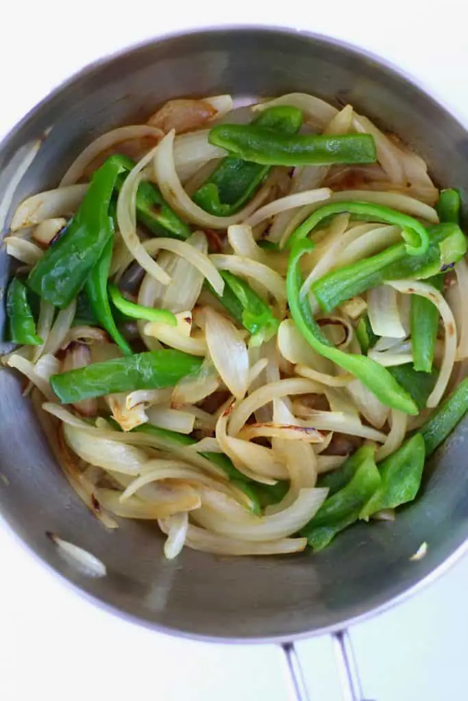Sliced onion and green pepper in a silver pan against a white background