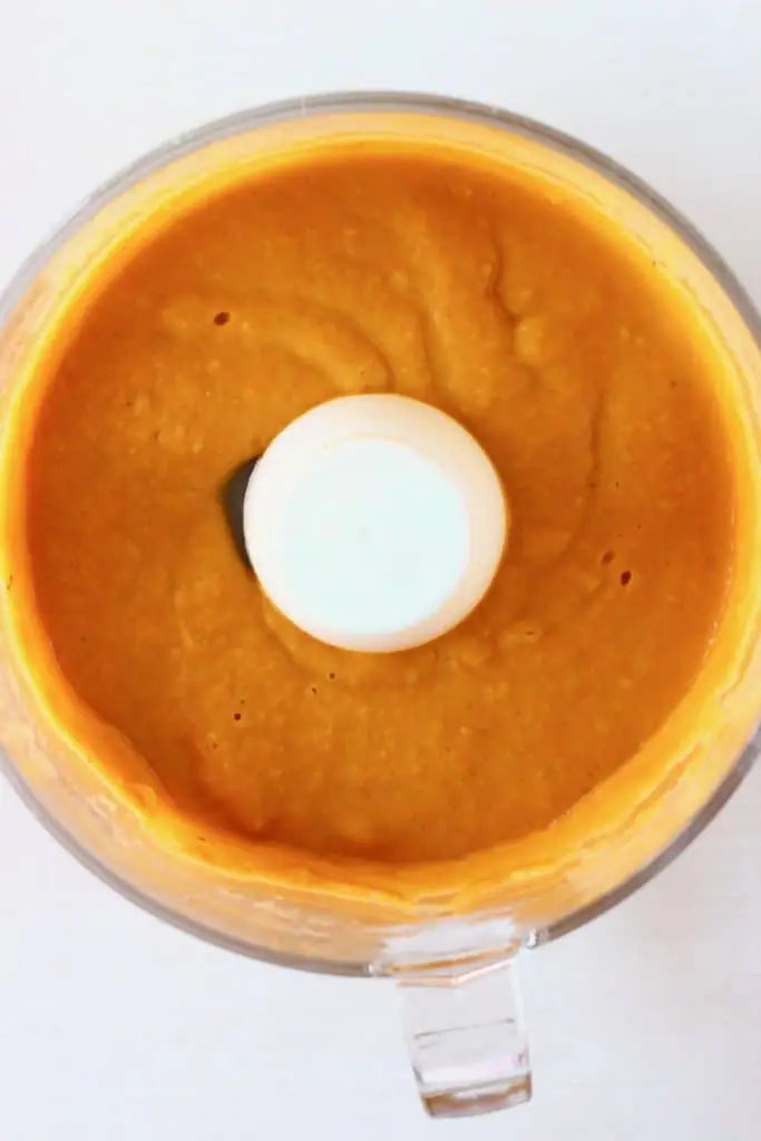 An orange vegan queso in a food processor against a white background