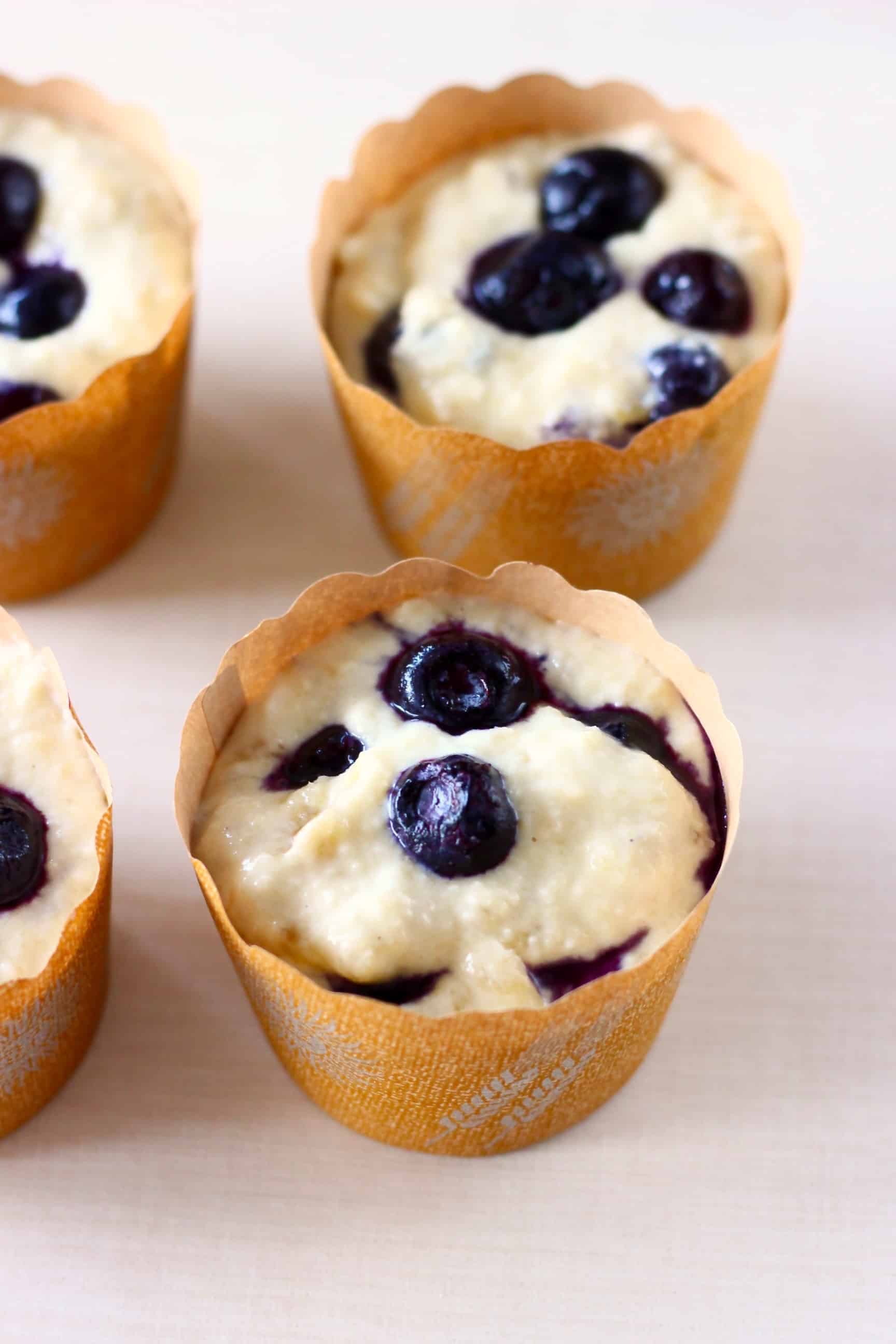 Raw gluten-free vegan blueberry banana muffin batter with blueberries in four paper muffin cases 