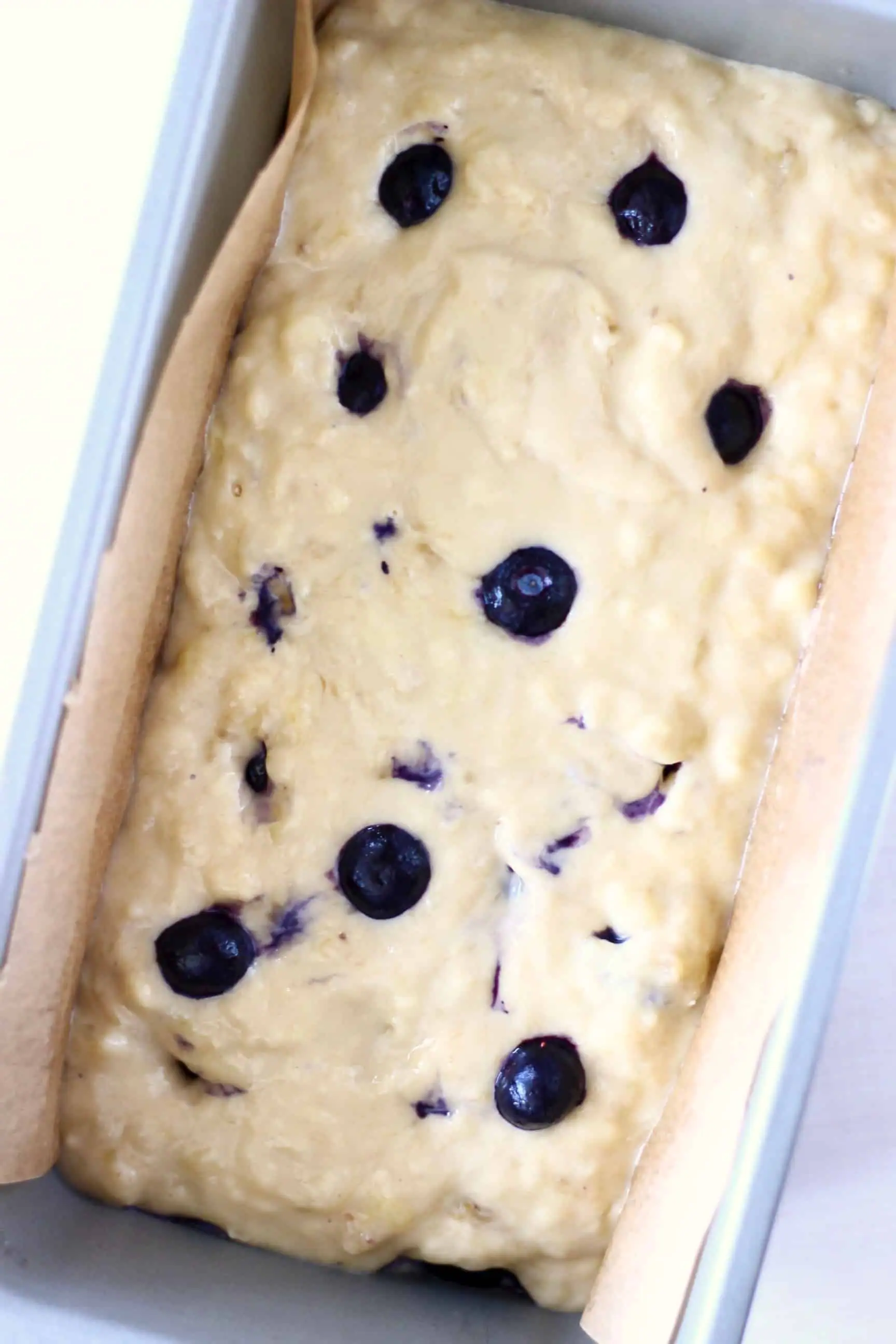 Gluten-free vegan banana bread batter with blueberries in a loaf tin lined with baking paper
