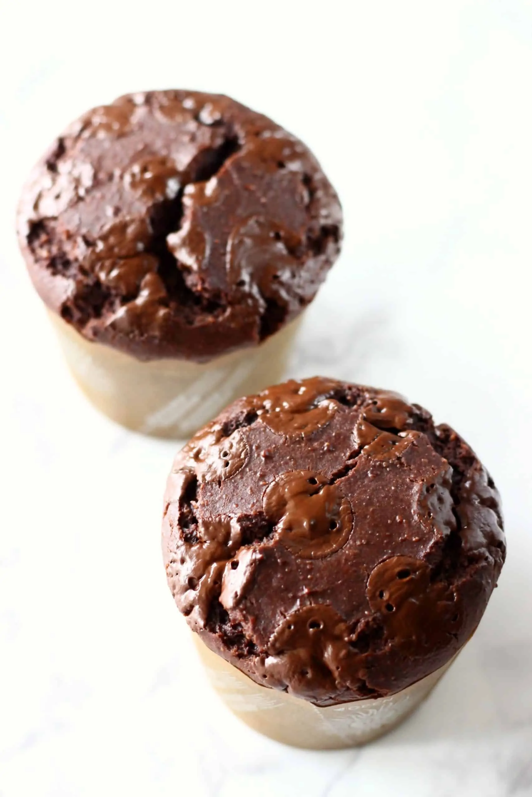 Two gluten-free vegan chocolate muffins in brown muffin cases topped with chocolate chips