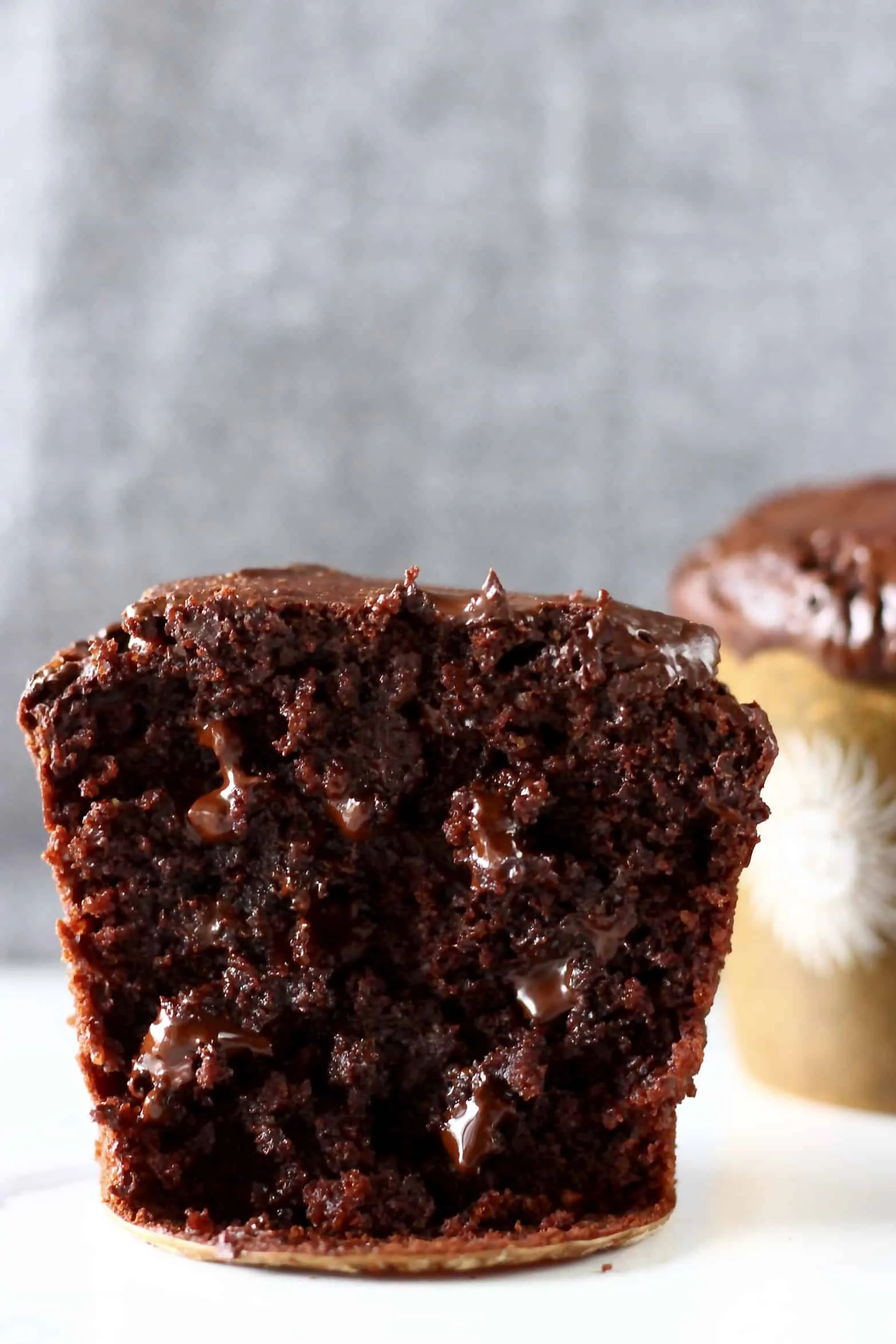 Two gluten-free vegan chocolate muffins with chocolate chips, one cut in half