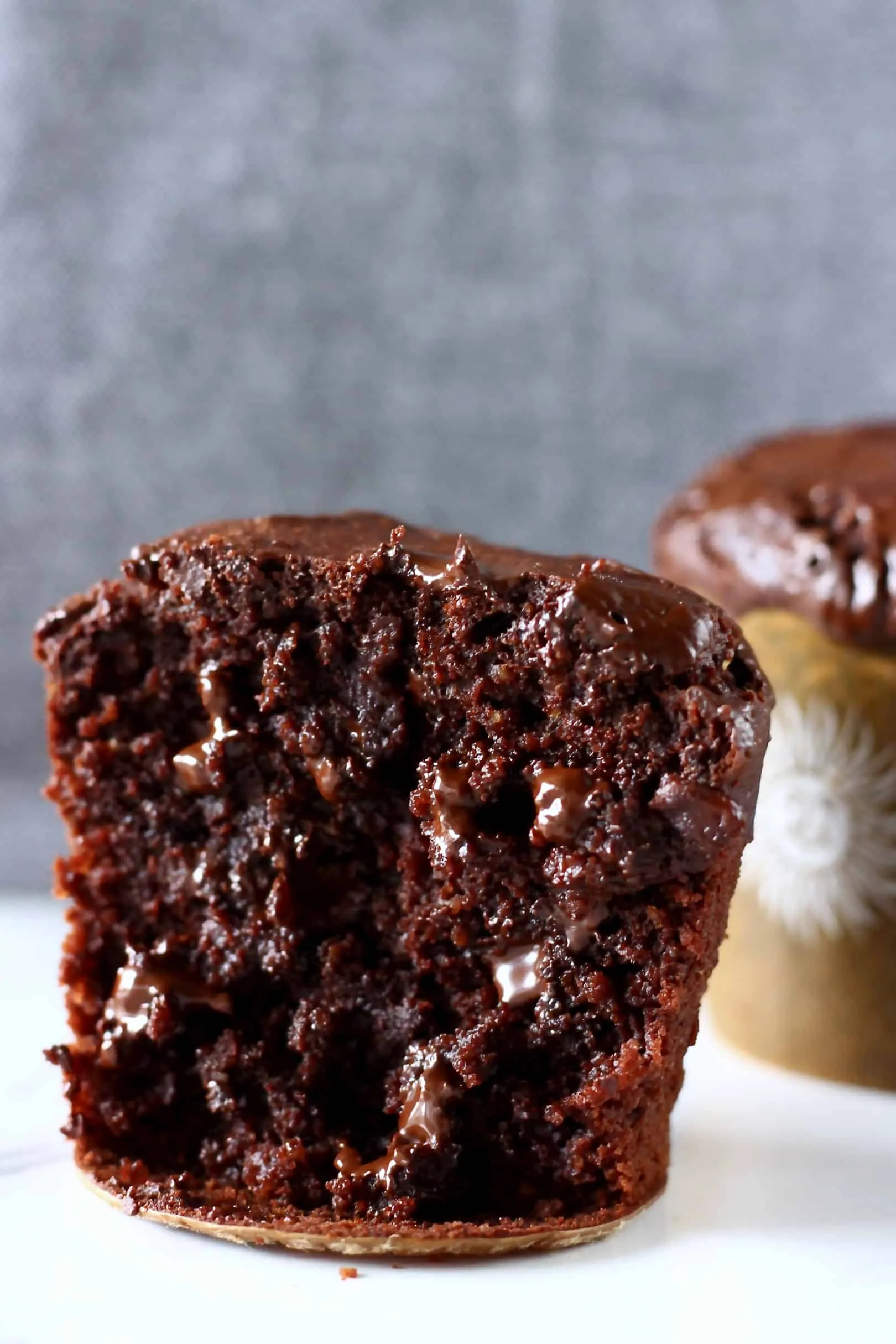 Two gluten-free vegan chocolate muffins with chocolate chips, one cut in half