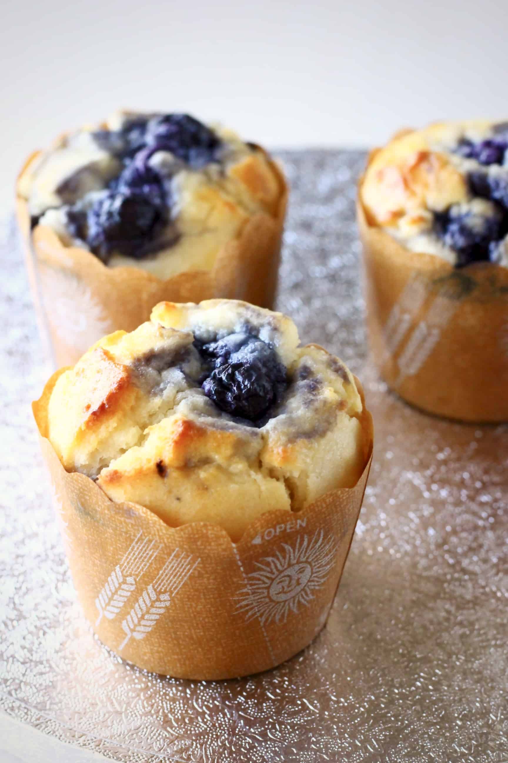 Three vegan blueberry muffins in brown muffin cases on a silver background
