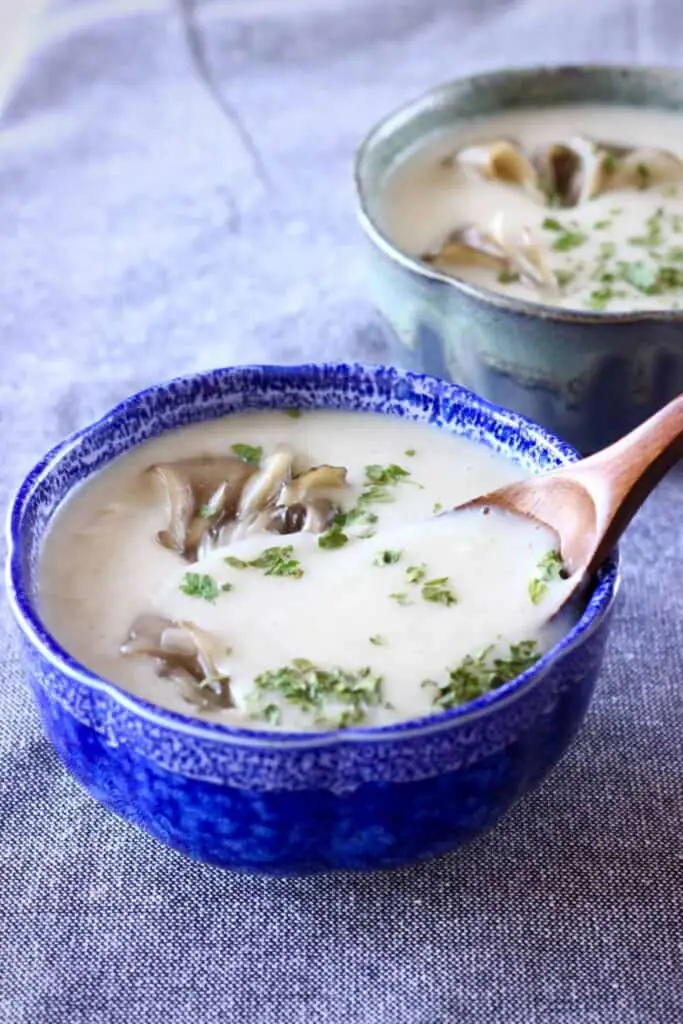 Two blue bowls filled with a beige-coloured mushroom soup with a wooden spoon sticking into one