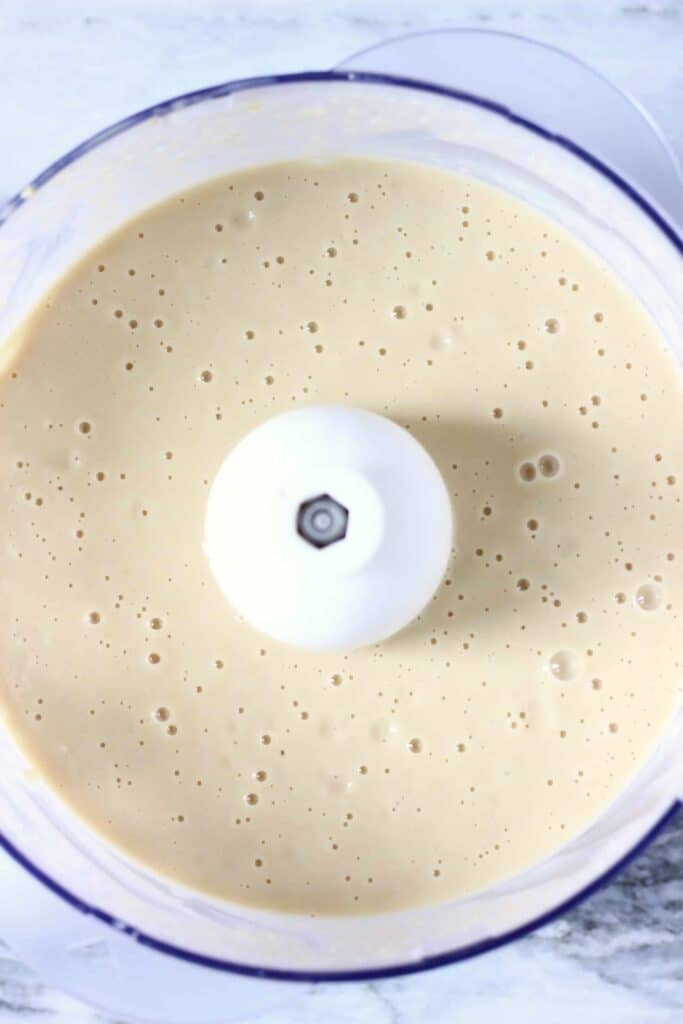 Photo of white sauce in a food processor against a marble background