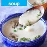 A small dark blue bowl of beige soup with a wooden spoon lifting up a mouthful of it against a grey background