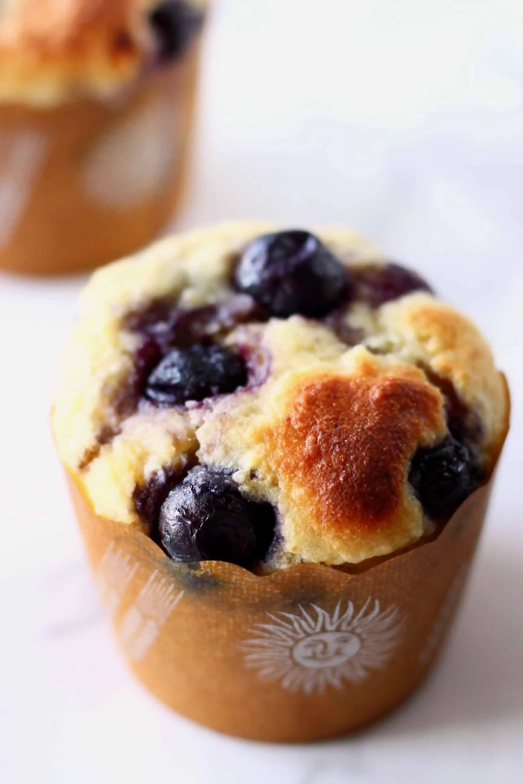 Two gluten-free vegan blueberry banana muffins in brown muffin cases 