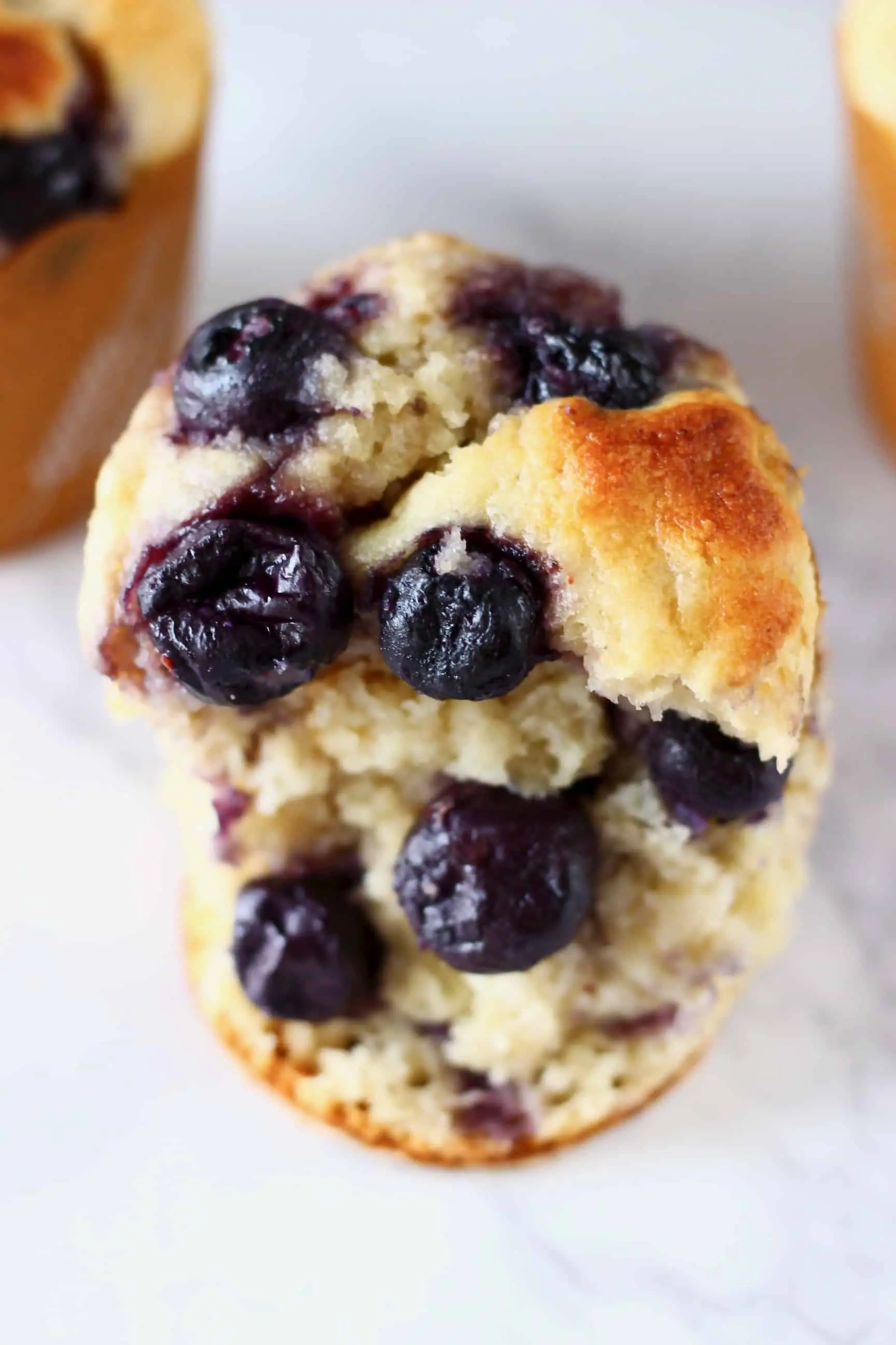 Half a gluten-free vegan blueberry banana muffin with two more muffins in the background