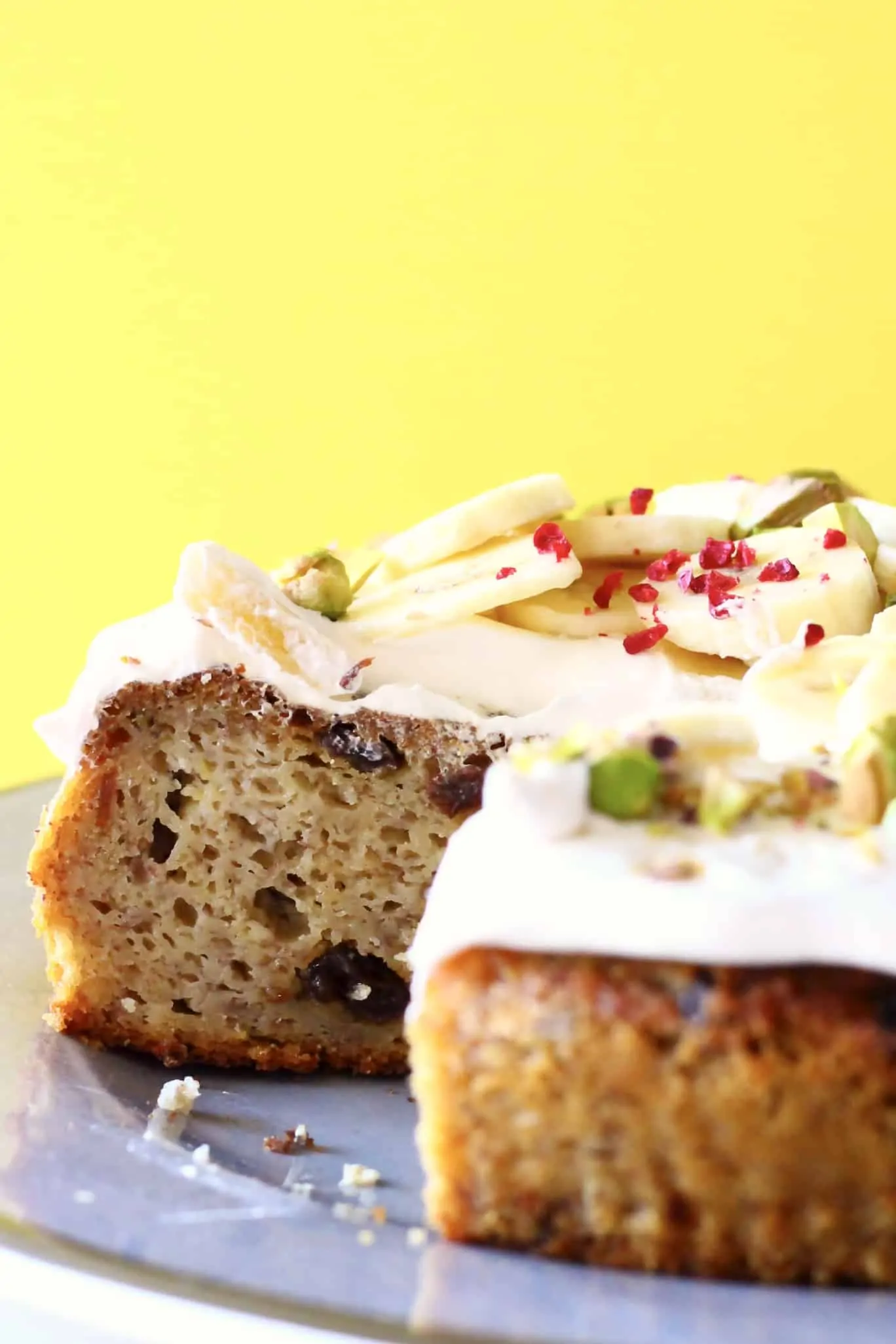 Sliced gluten-free vegan banana cake with raisins topped with vegan cream cheese frosting and sliced bananas