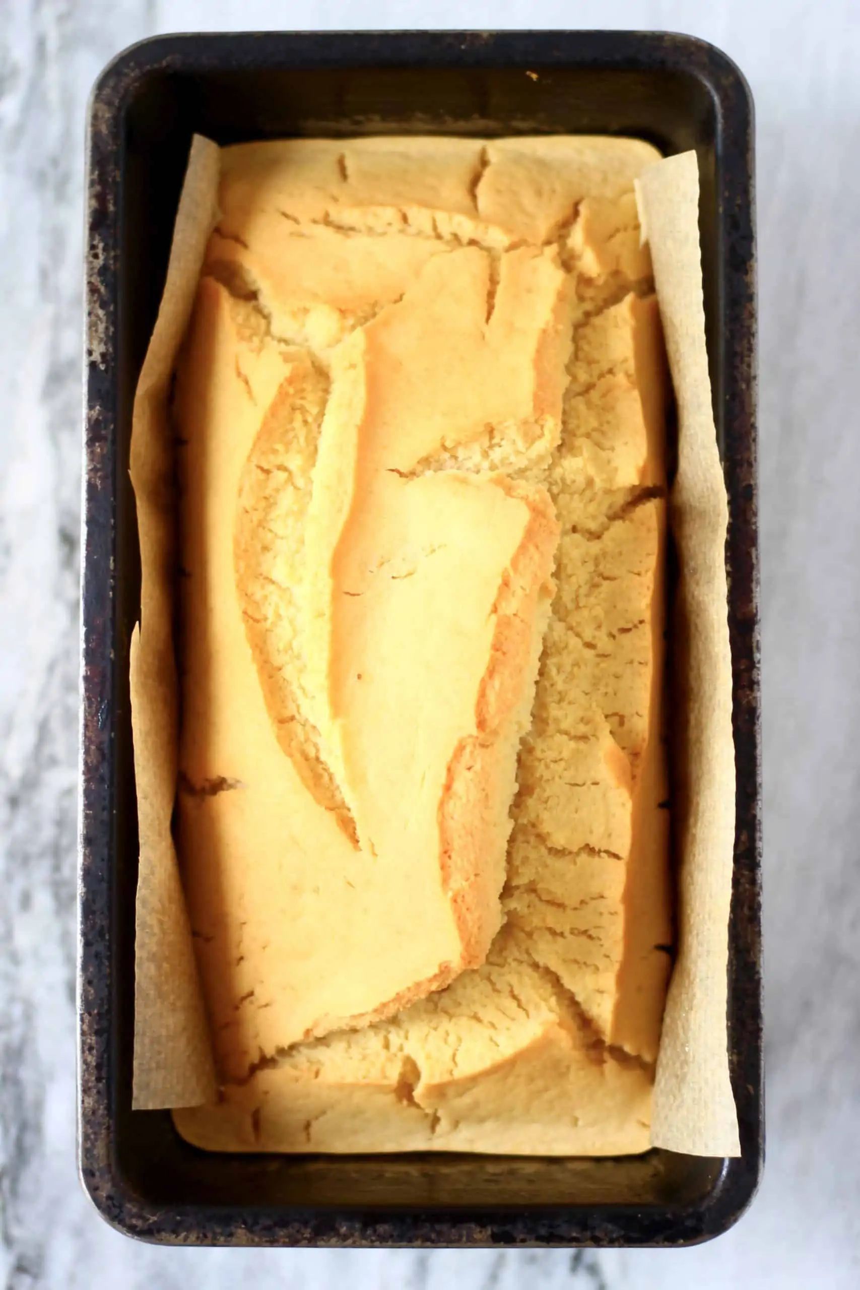 A loaf of gluten-free vegan bread in a loaf tin lined with baking paper