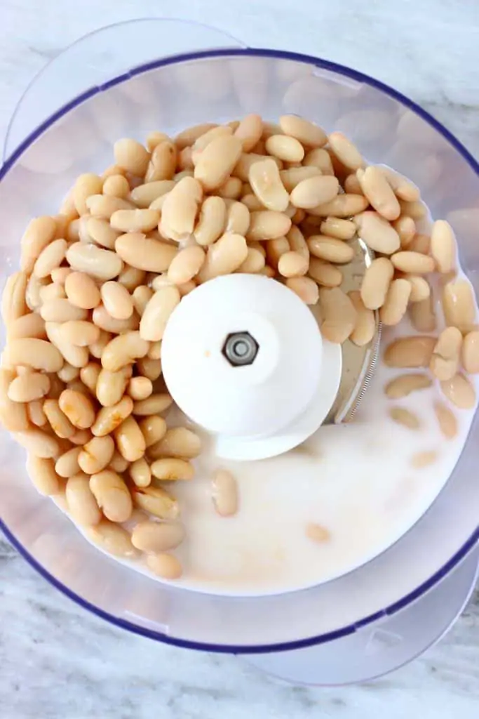 White beans and almond milk in a food processor against a marble background