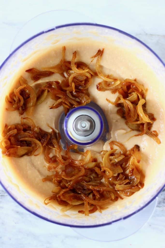 Creamy white dip and caramelised onions in a food processor against a marble background 