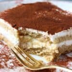 A square of gluten-free vegan tiramisu on a plate with a mouthful cut out of it
