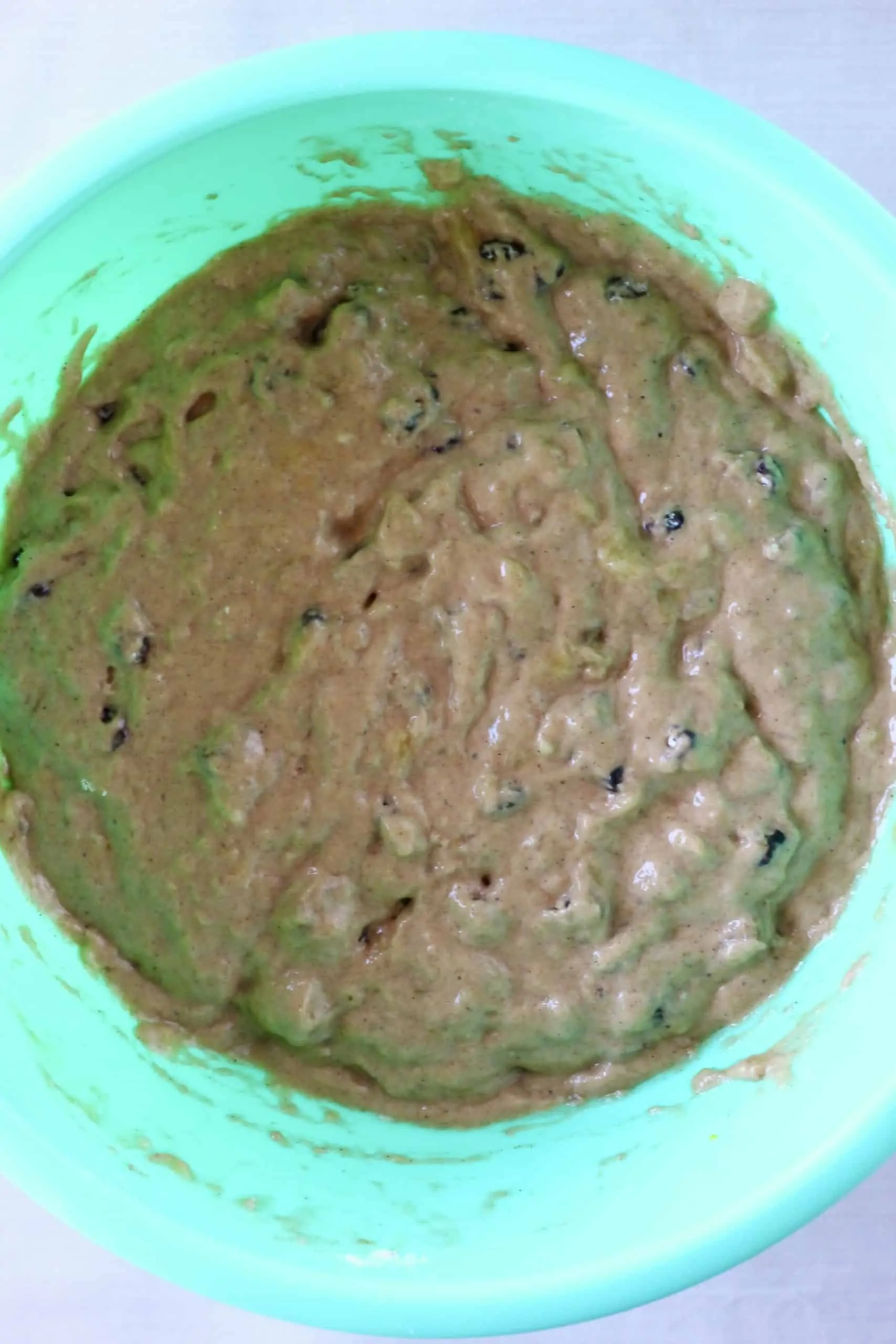Raw gluten-free vegan banana cake batter with raisins in a mixing bowl