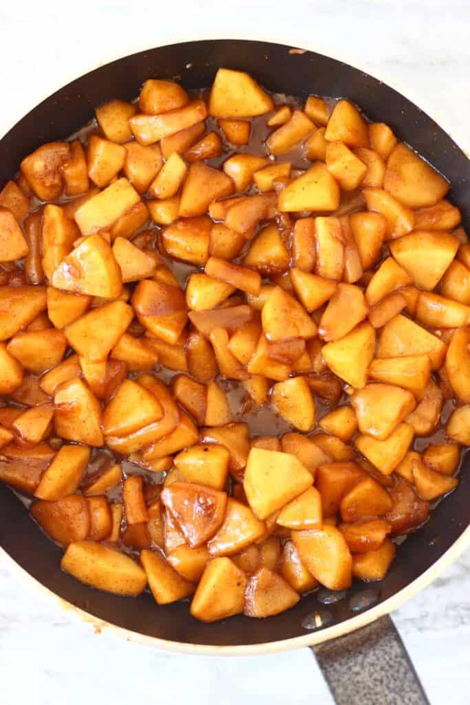 Photo of chopped apple pieces with cinnamon and brown sugar in a black frying pan