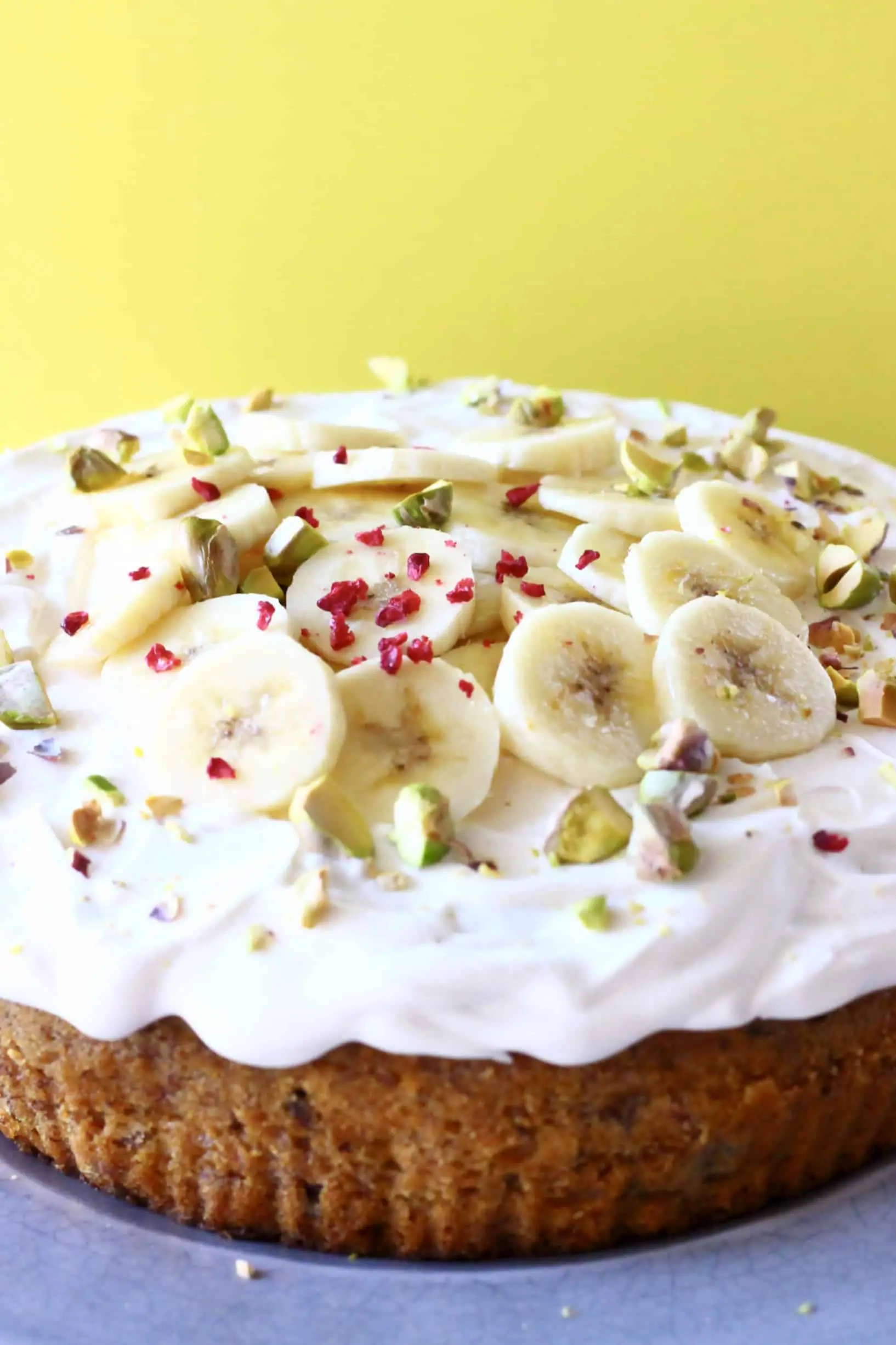 A gluten-free vegan banana cake topped with vegan cream cheese  frosting and sliced bananas
