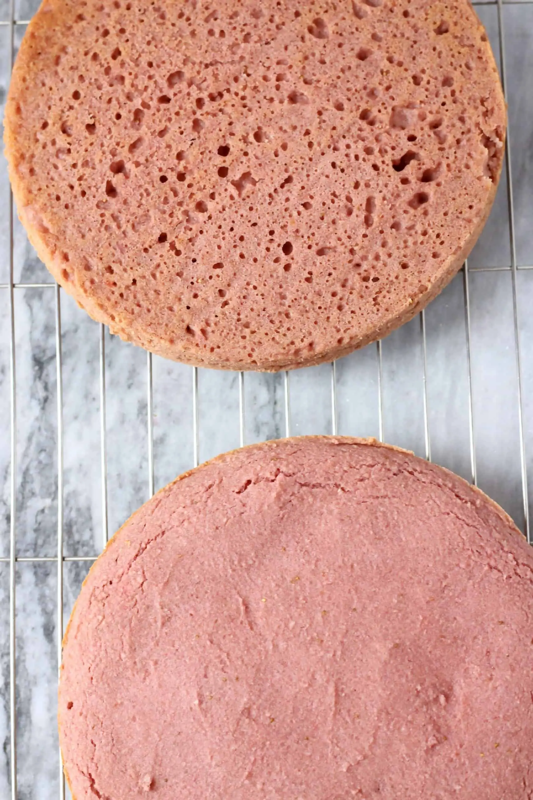 Two round pink gluten-free vegan strawberry cake sponges on a wire rack