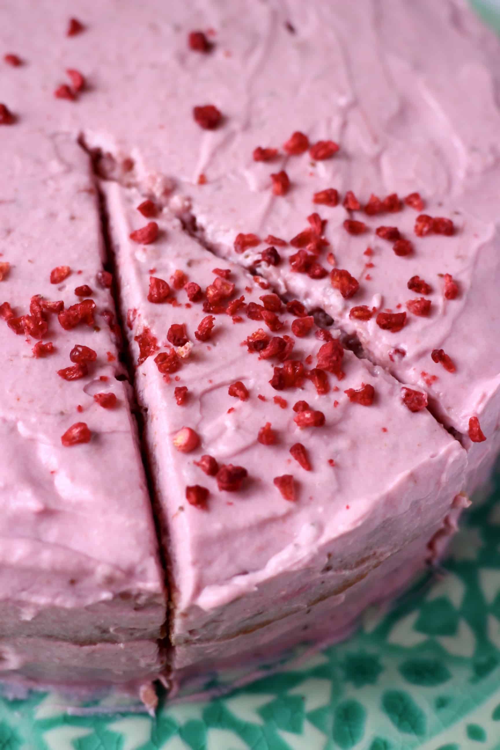 A pink gluten-free vegan strawberry cake with pink strawberry frosting with a slice cut 