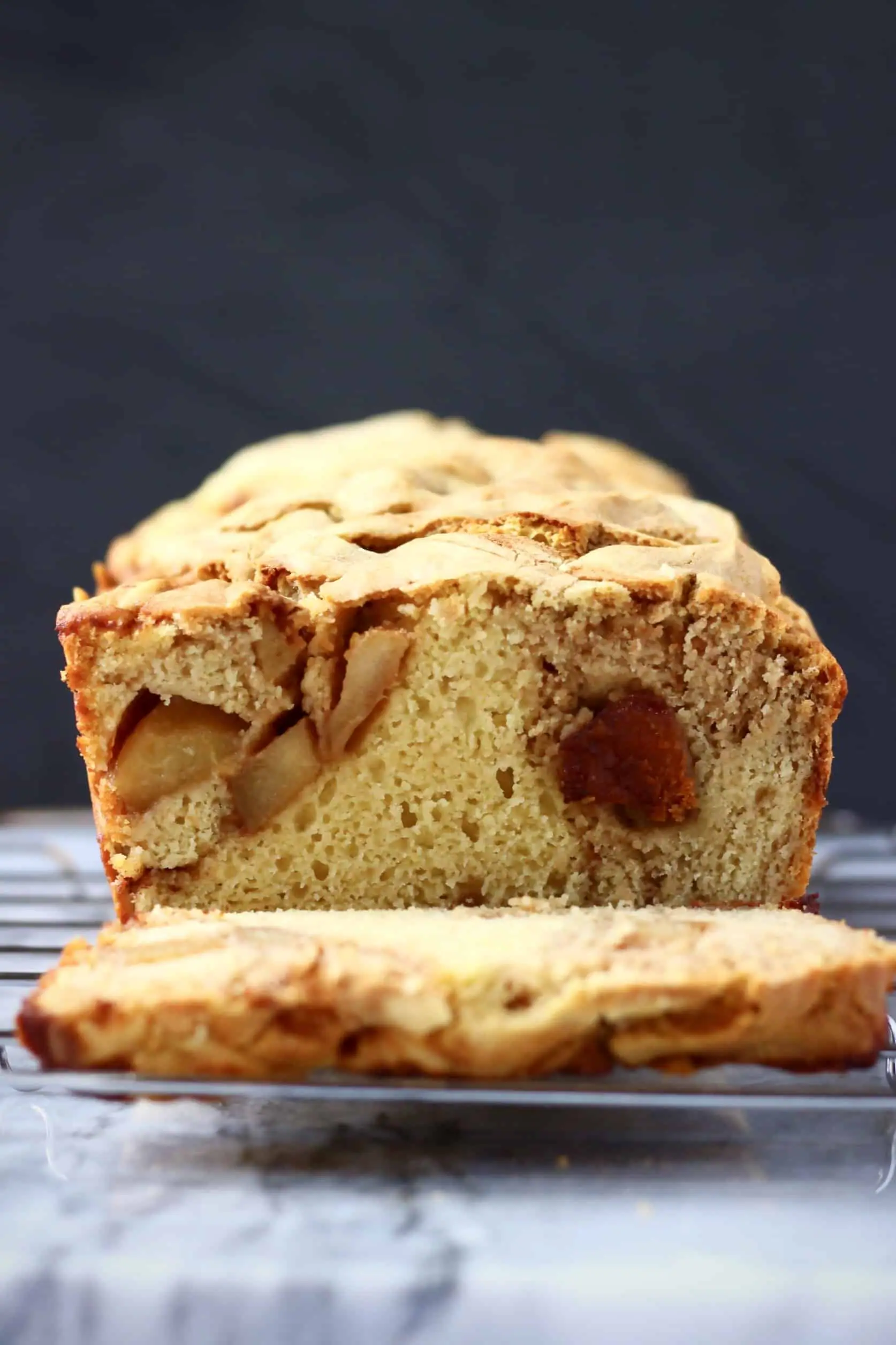 A loaf of vegan apple bread on a wire rack with a slice next to it