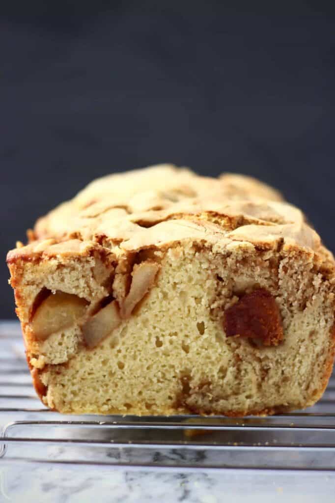 Photo of a sliced loaf of apple bread on a silver wire rack on a marble slab against a black background