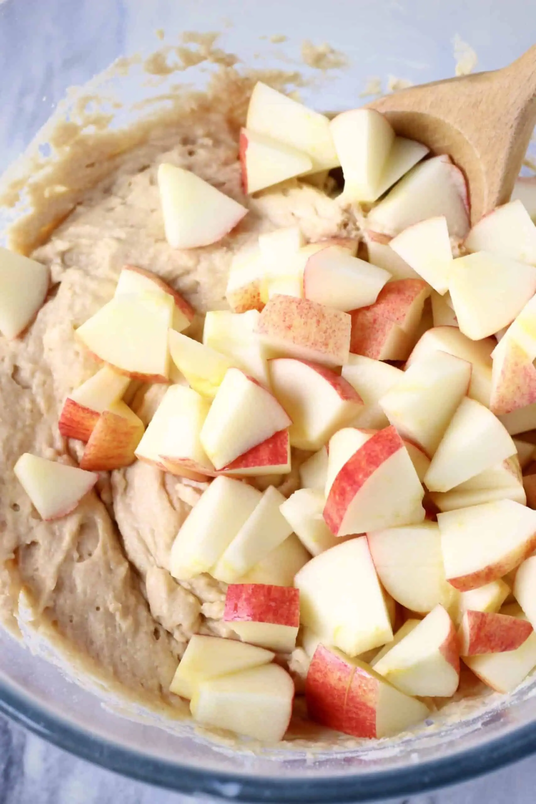 Raw gluten-free vegan muffin batter with pieces of chopped apple in a bowl with a wooden spoon