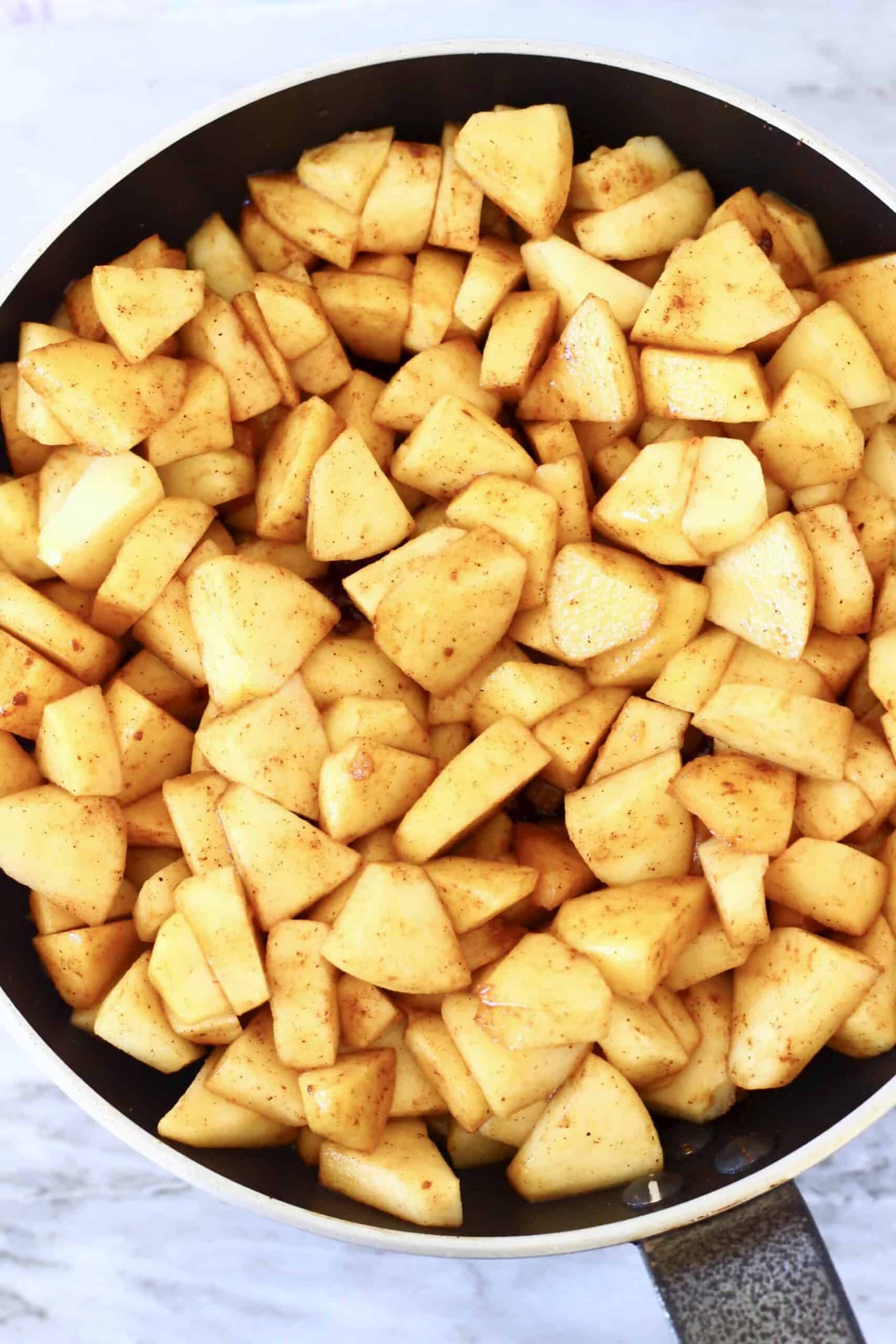 Photo of chopped apple pieces with cinnamon and brown sugar in a black frying pan