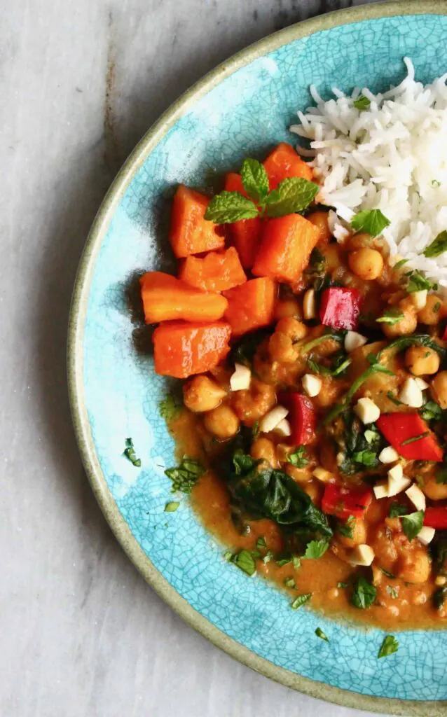 Chickpeas in a red curry sauce next to a pile of white rice on a blue plate against a marble background