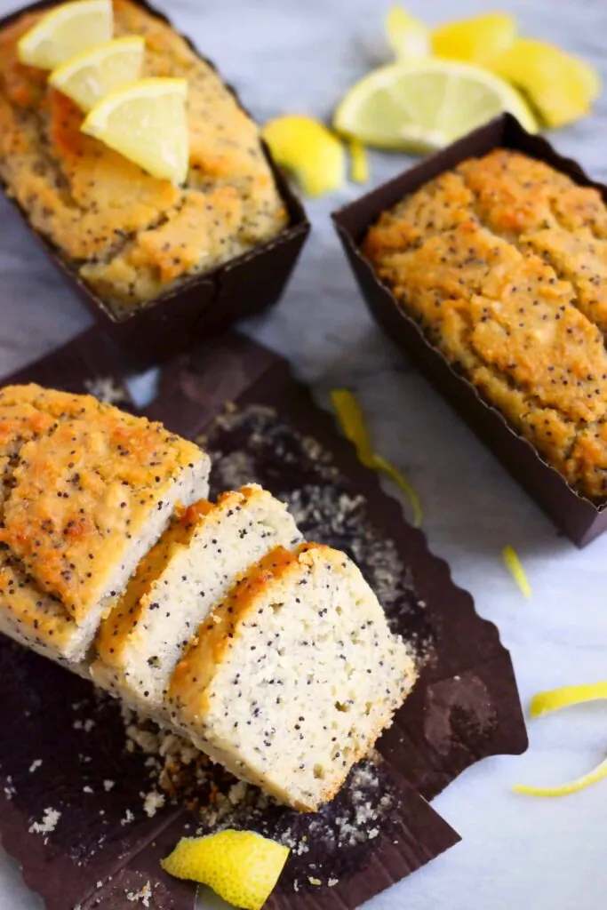 Three lemon poppy seed loaf cakes against a marble background, one sliced