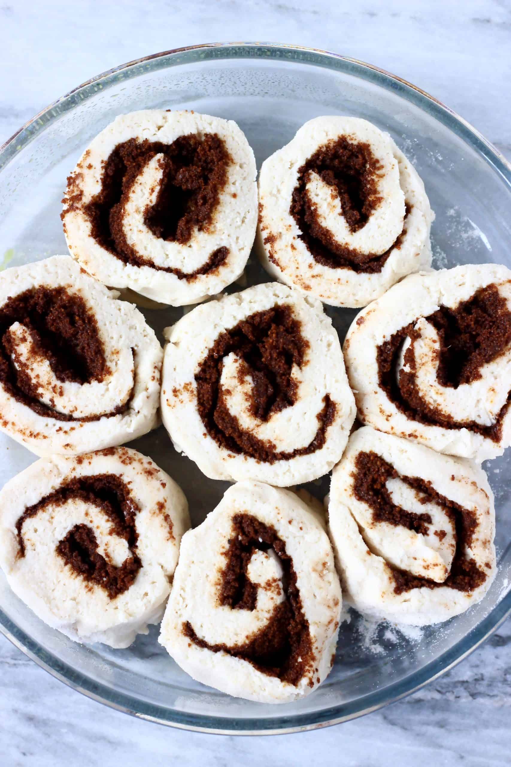 Eight raw gluten-free vegan cinnamon rolls in a round baking dish before proving