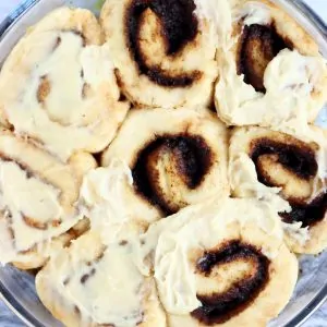 Seven gluten-free vegan cinnamon rolls in a round baking dish, topped with vegan cream cheese frosting