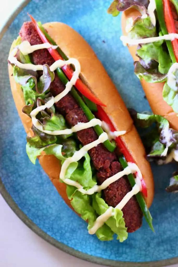 A hot dog with lettuce and sliced red peppers drizzled with mayonnaise on a blue plate