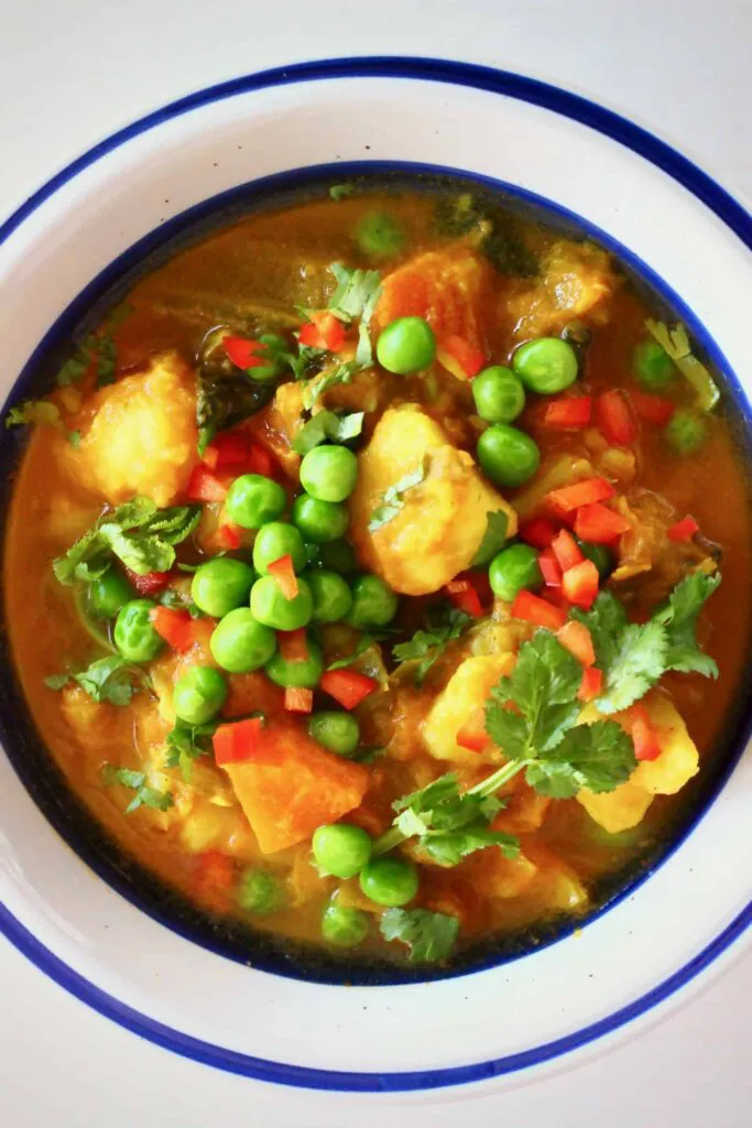 Diced potatoes and green peas in a red curry sauce in a white bowl with a dark blue rim against a white background