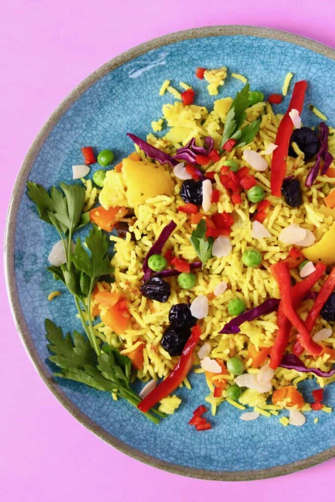 Yellow rice with vegetables on a blue plate against a pink background