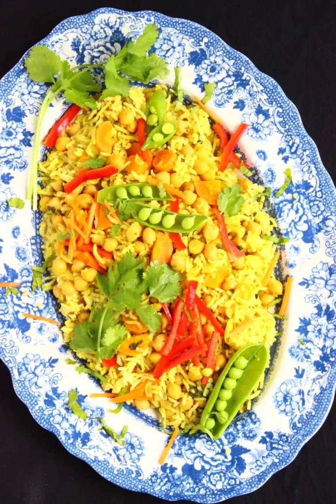 Yellow rice with vegetables in an oval-shaped blue plate against a black background