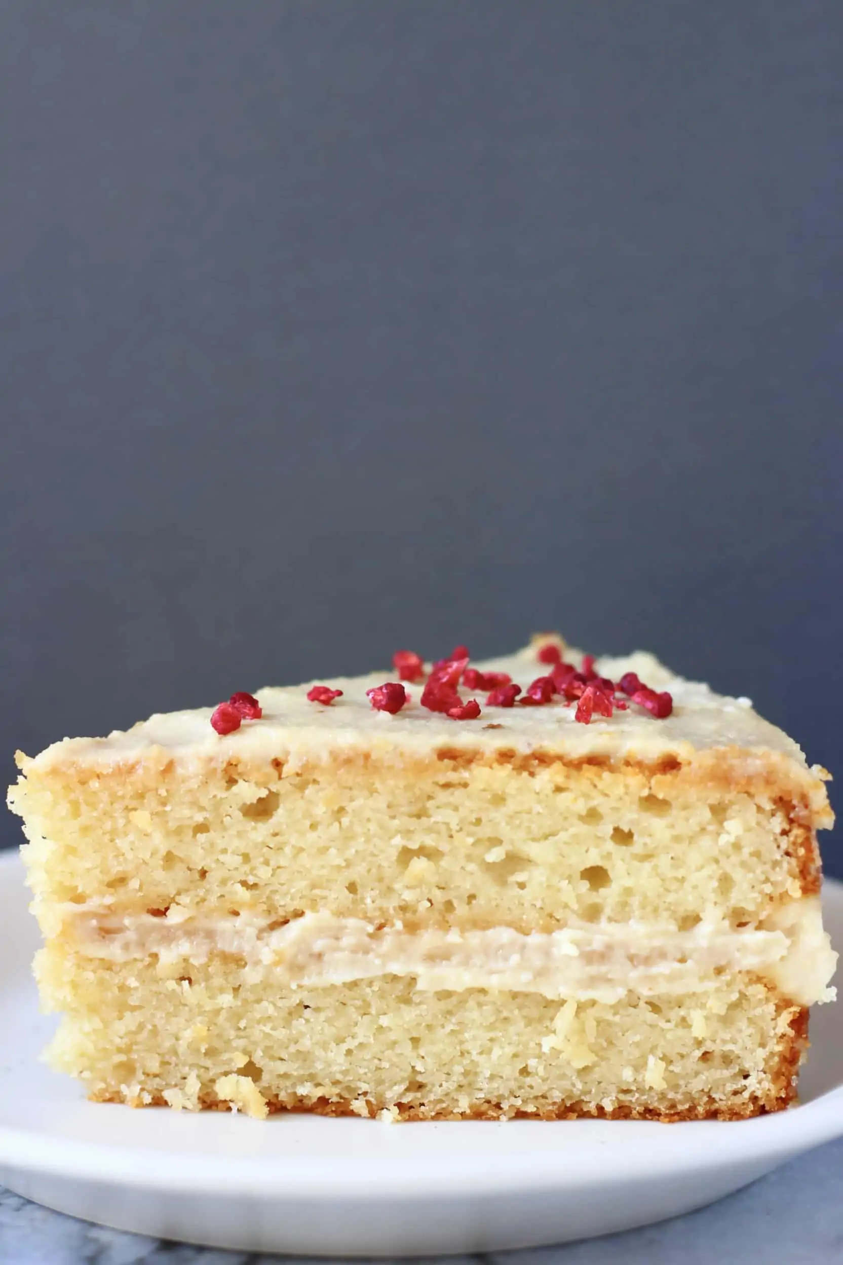 A slice of gluten-free vegan vanilla cake with buttercream on a plate