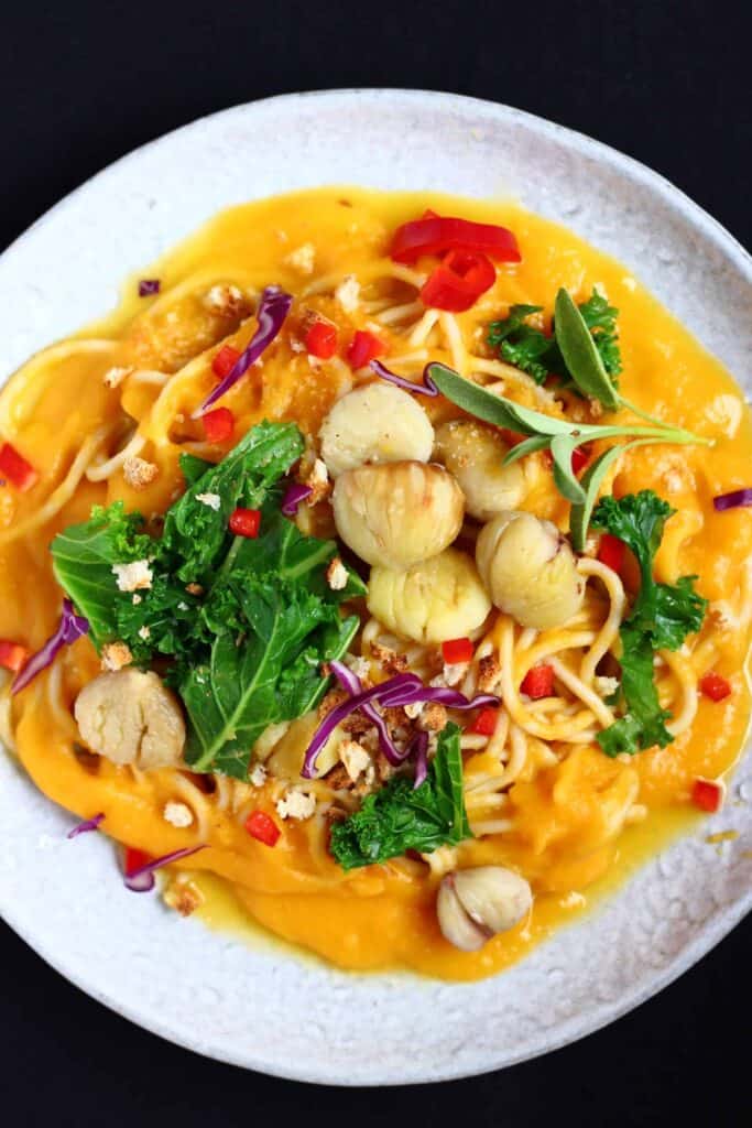 Spaghetti in a pumpkin sauce with kale and chestnuts on a grey plate against a black background