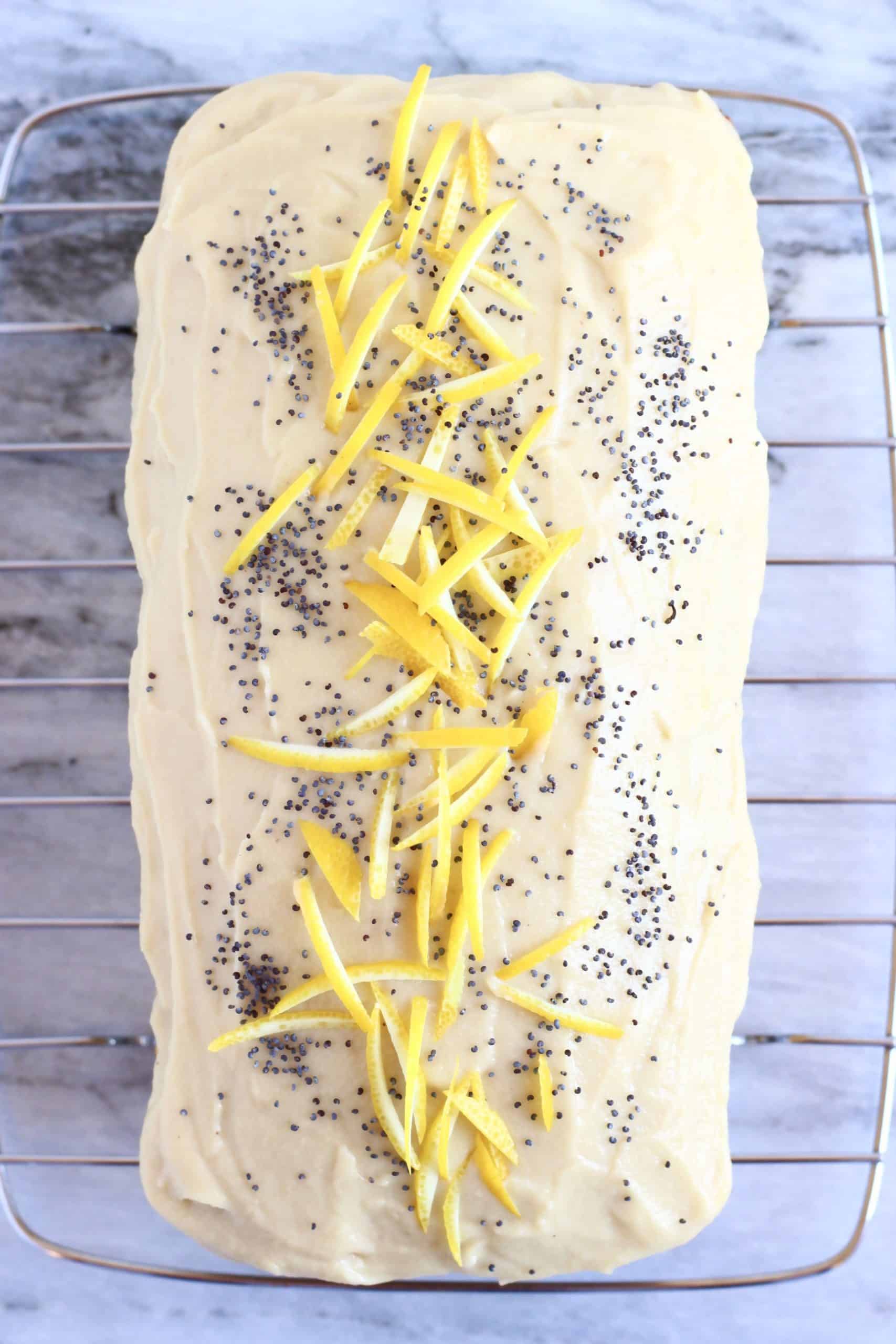 Gluten-free vegan lemon poppy seed cake loaf topped with vegan lemon frosting, lemon zest and poppy seeds on a wire rack