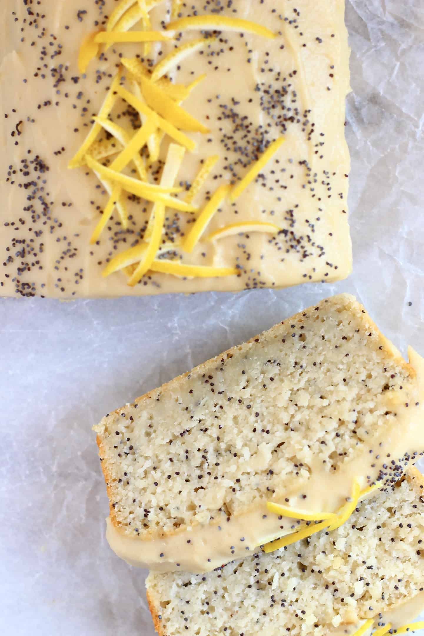 Gluten-free vegan lemon poppy seed cake loaf topped with frosting, lemon zest and poppy seeds with two slices next to it