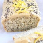 Gluten-free vegan lemon poppy seed cake topped with frosting, lemon zest and poppy seeds with two slices next to it