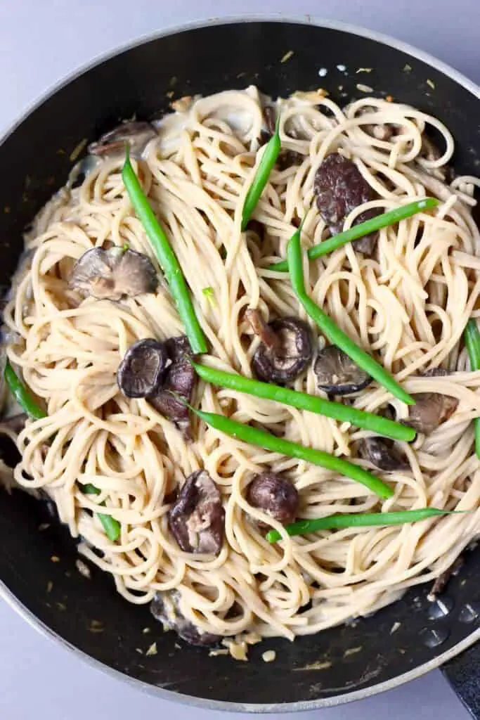 Spaghetti with mushrooms and green beans in a black frying pan against a grey background