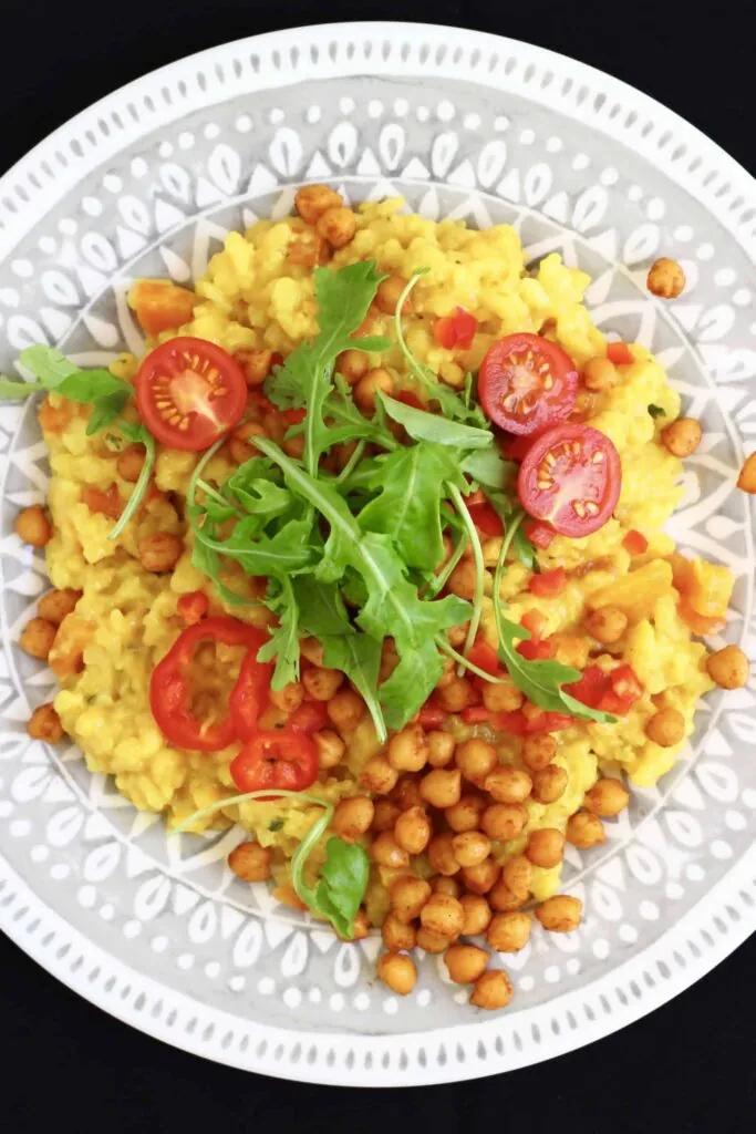 Yellow rice with cherry tomatoes and green rocket with brown chickpeas on a grey plate against a black background