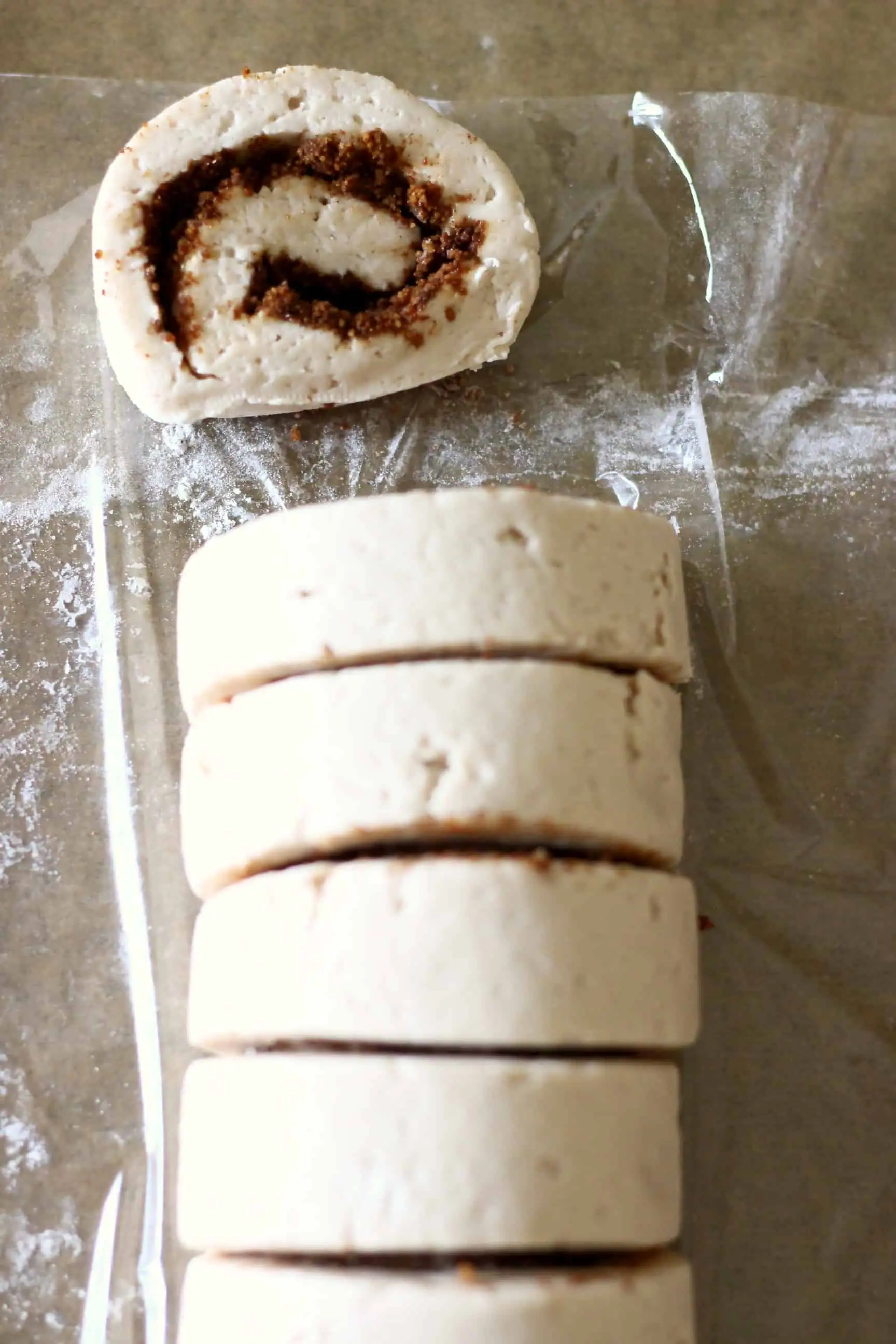 A roll of gluten-free vegan cinnamon roll dough filled with cinnamon sugar being cut into pieces 