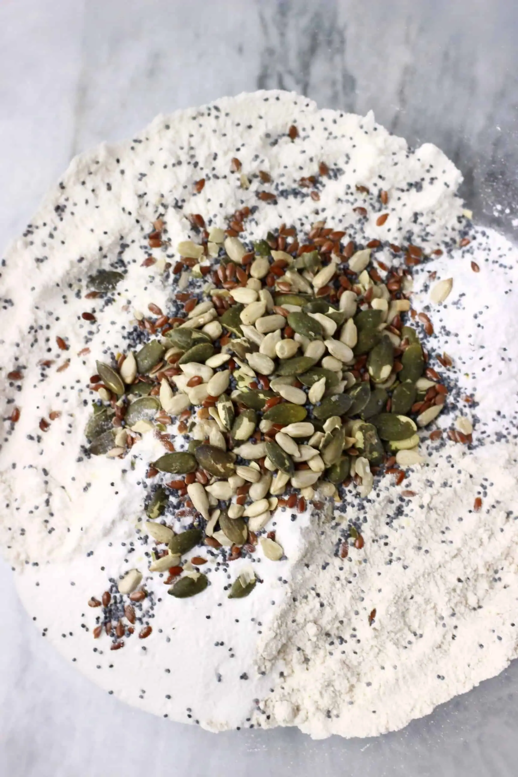 Flour, poppy seeds, flax seeds, sunflower seeds and pumpkin seeds in a glass mixing bowl 