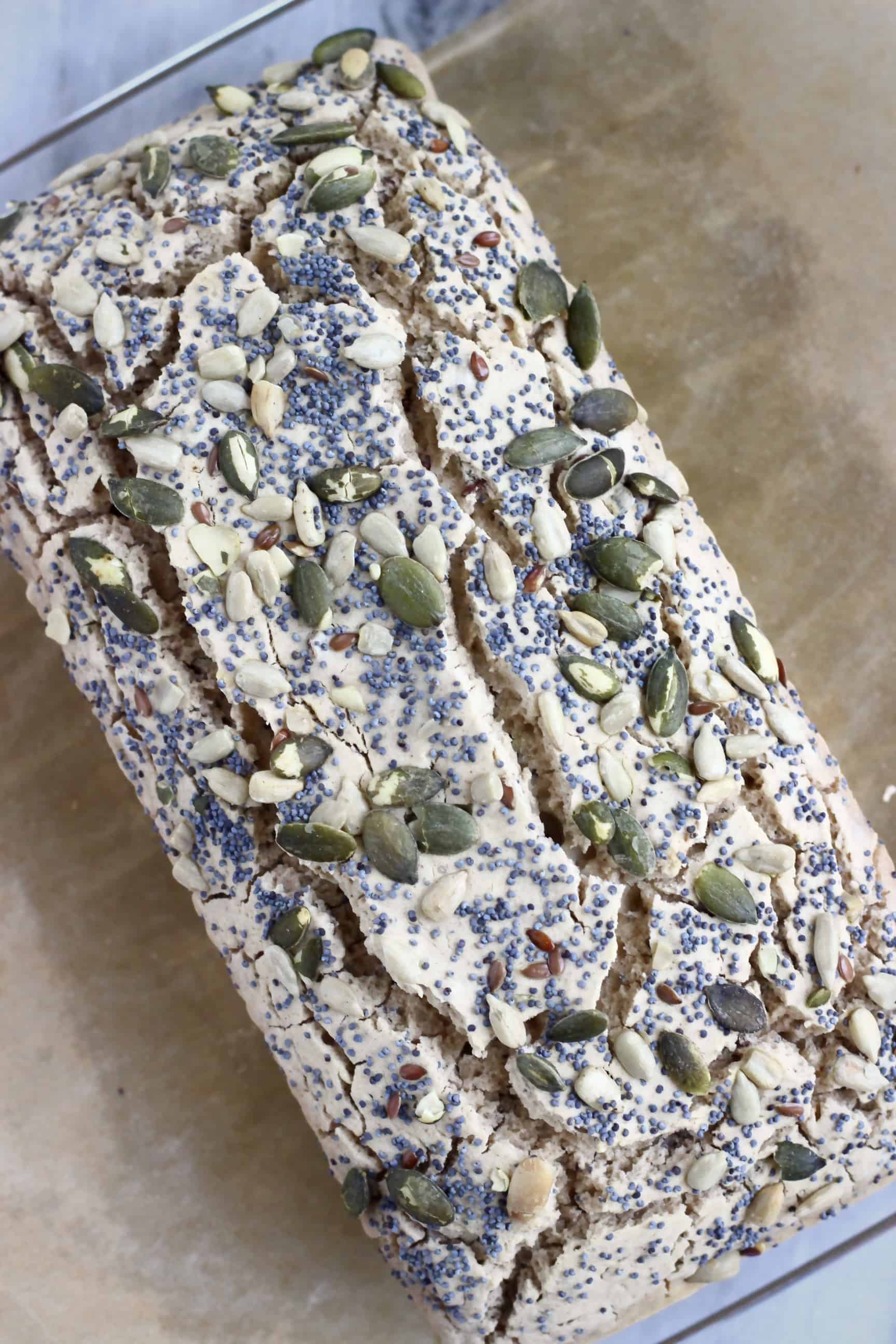 A loaf of Gluten-Free Vegan Seeded Buckwheat Bread on a sheet of brown baking paper