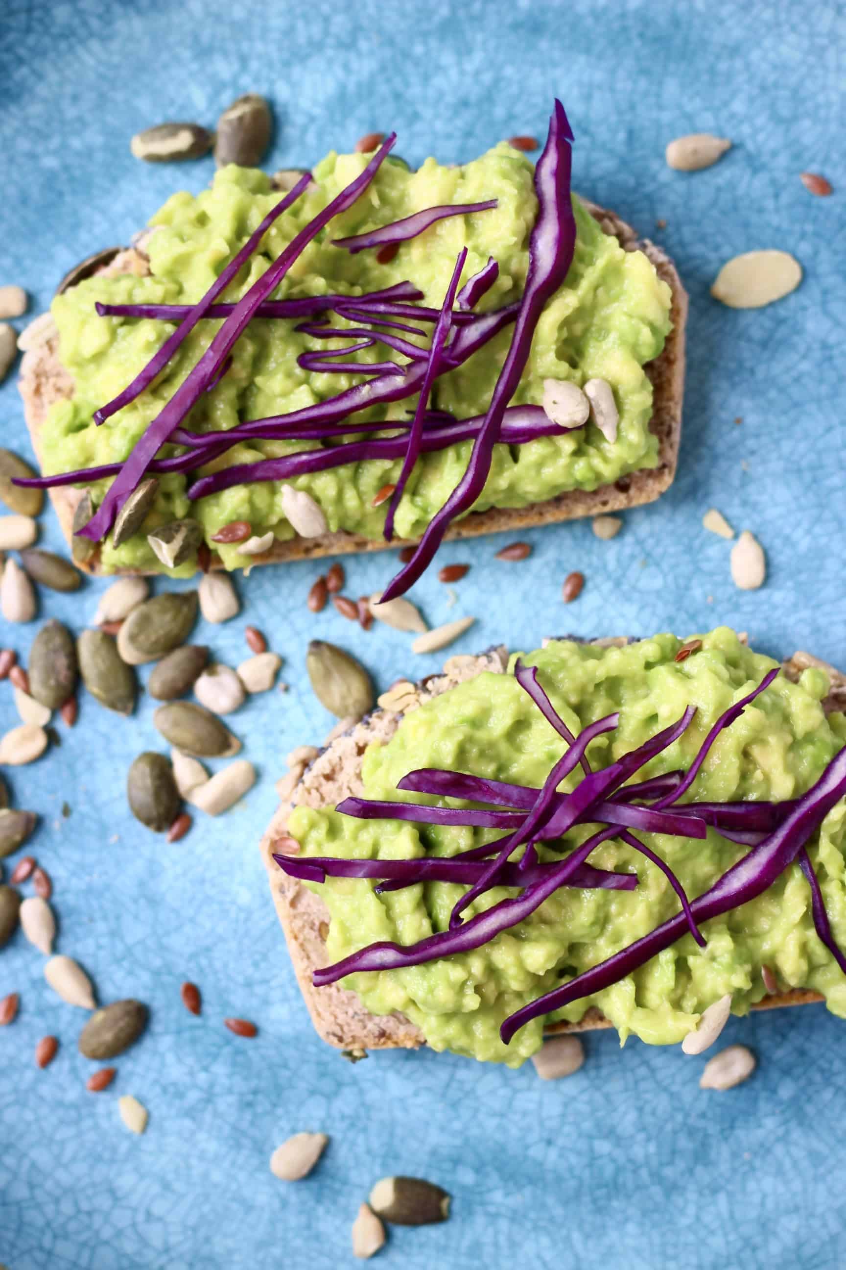 Two slices of Gluten-Free Vegan Seeded Buckwheat Bread topped with mashed avocado and shredded purple cabbage on a blue plate 