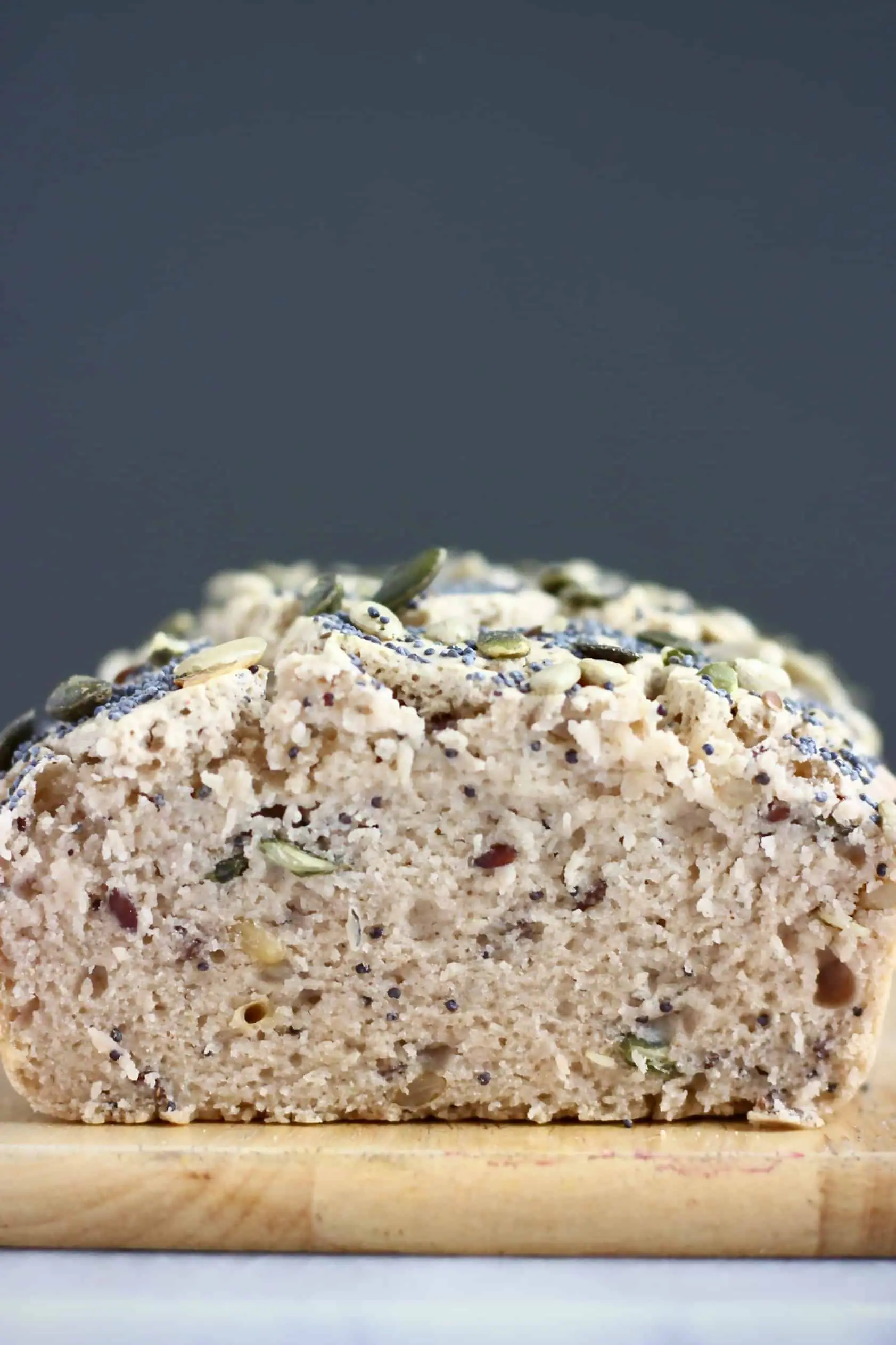 A sliced loaf of Gluten-Free Vegan Seeded Buckwheat Bread on a chopping board against a dark grey background