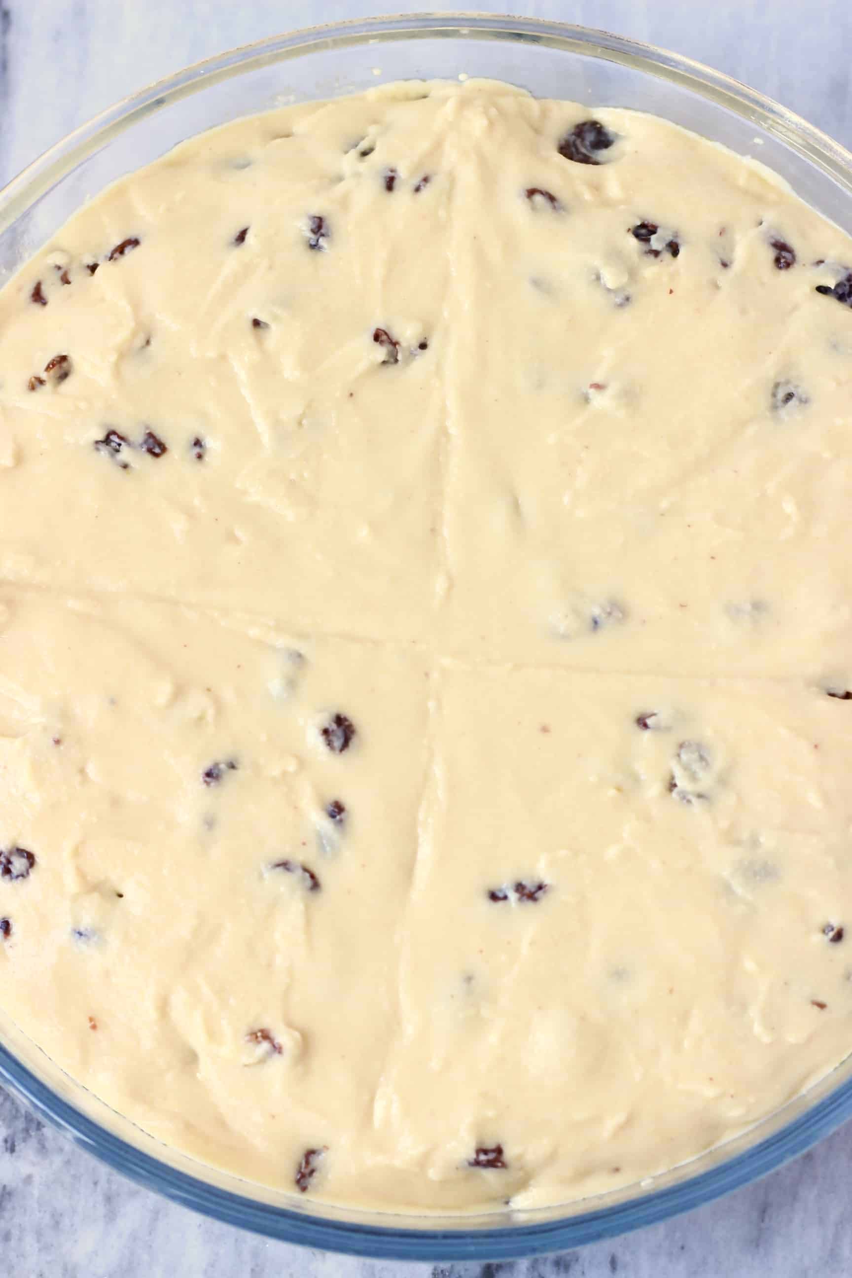 Gluten-Free Vegan Irish Soda Bread batter with raisins in a round glass baking dish with a cross marked on top