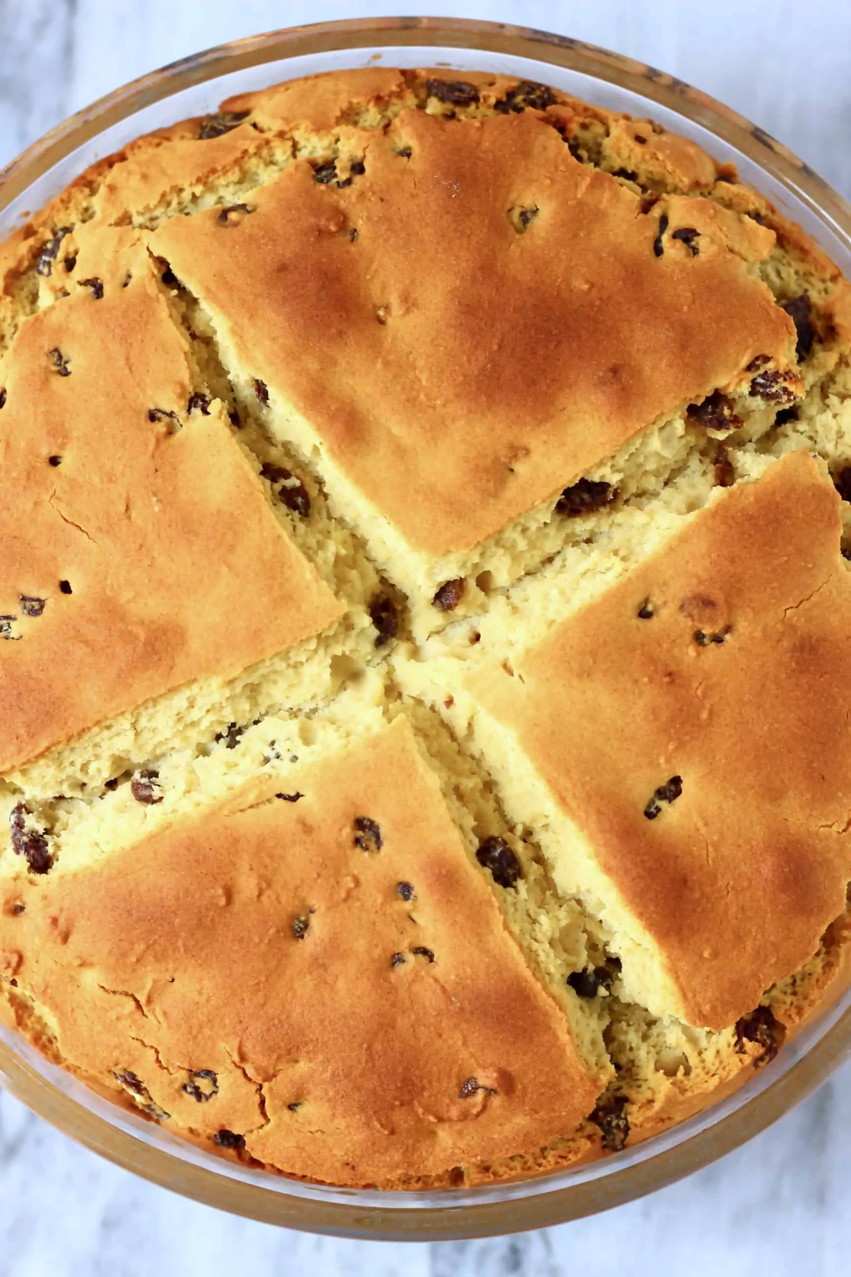 A round loaf of Gluten-Free Vegan Irish Soda Bread with a cross on top in a glass baking dish