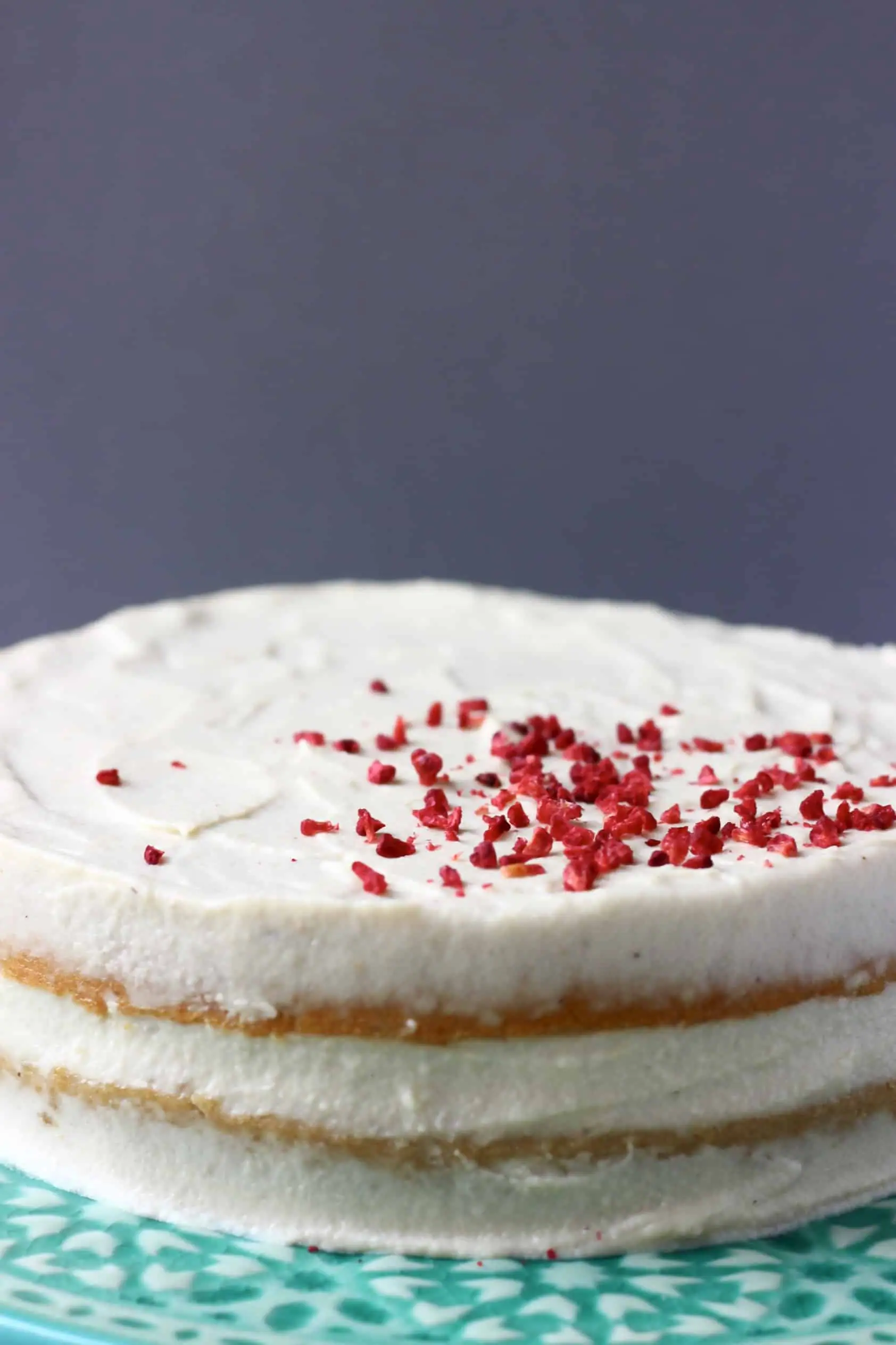 Gluten-free vegan vanilla cake covered with white frosting topped with freeze-dried raspberries 